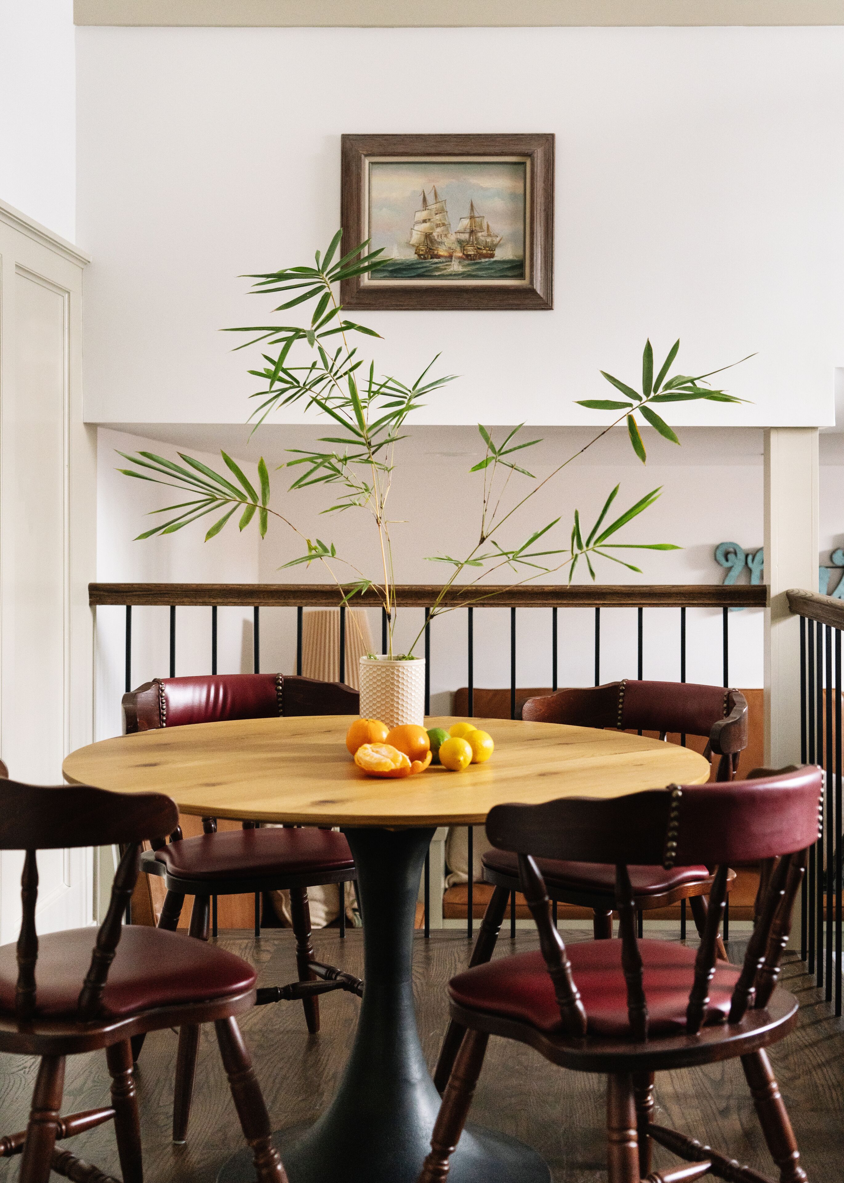 Zona pranzo con un tavolo rotondo in legno circondato da quattro sedie, una pianta in vaso e un quadro appeso al muro.