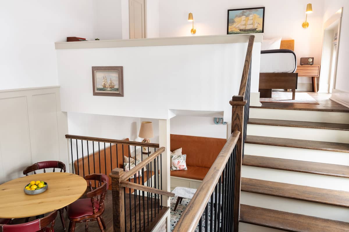 A staircase with wooden steps and a railing, leading to a bedroom with a bed and a nightstand.