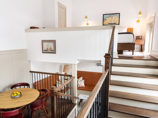 A staircase with wooden steps and a railing, leading to a bedroom with a bed and a nightstand.