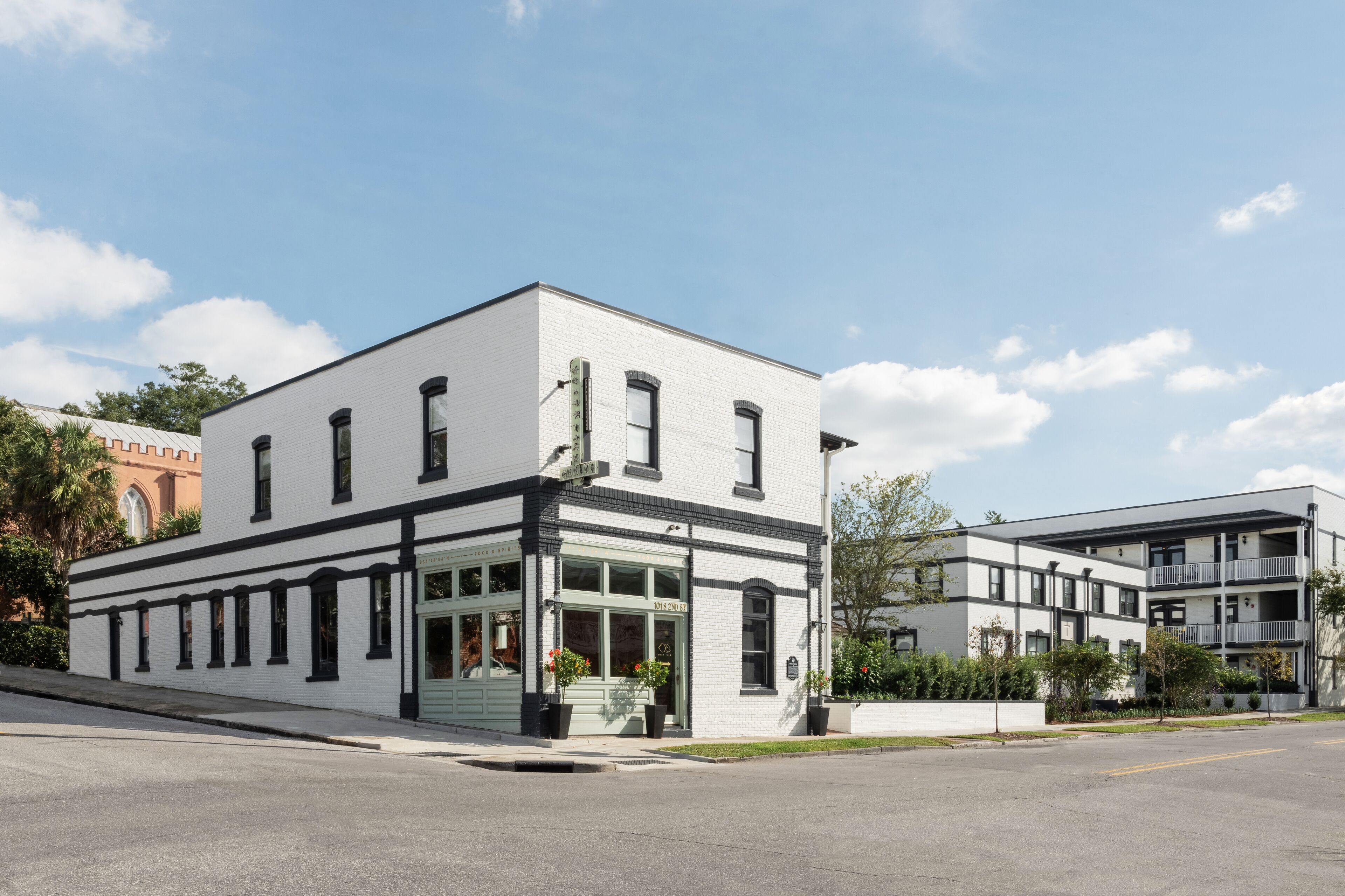 A two-story building with a white facade and black trim, featuring large windows and a ground-level entrance with a planter.