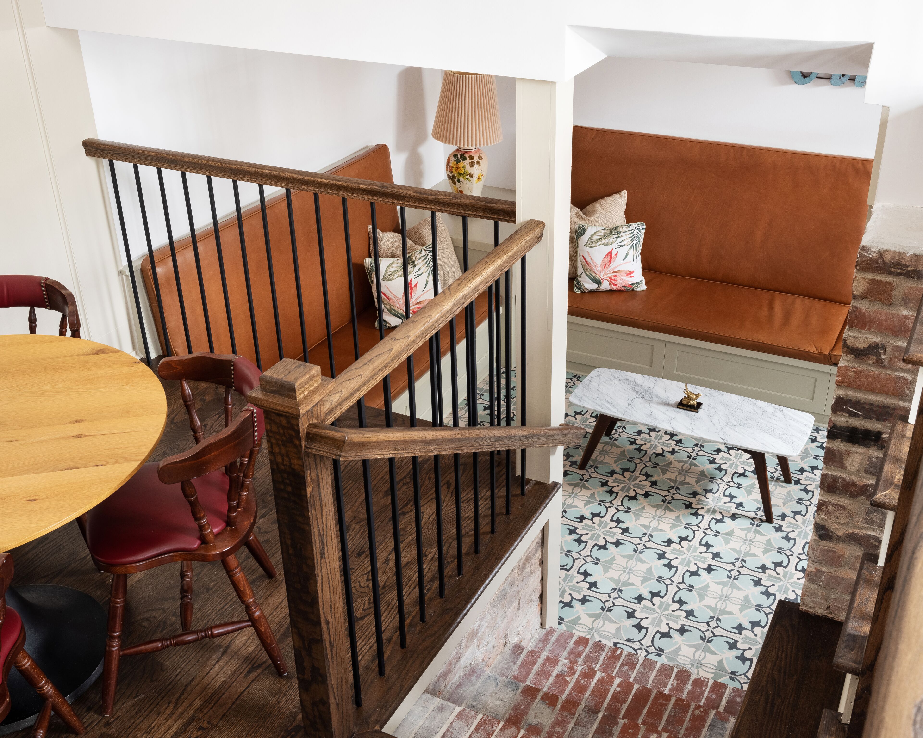 A staircase with wooden railings, a red cushioned bench, a wooden dining table, and a patterned floor.
