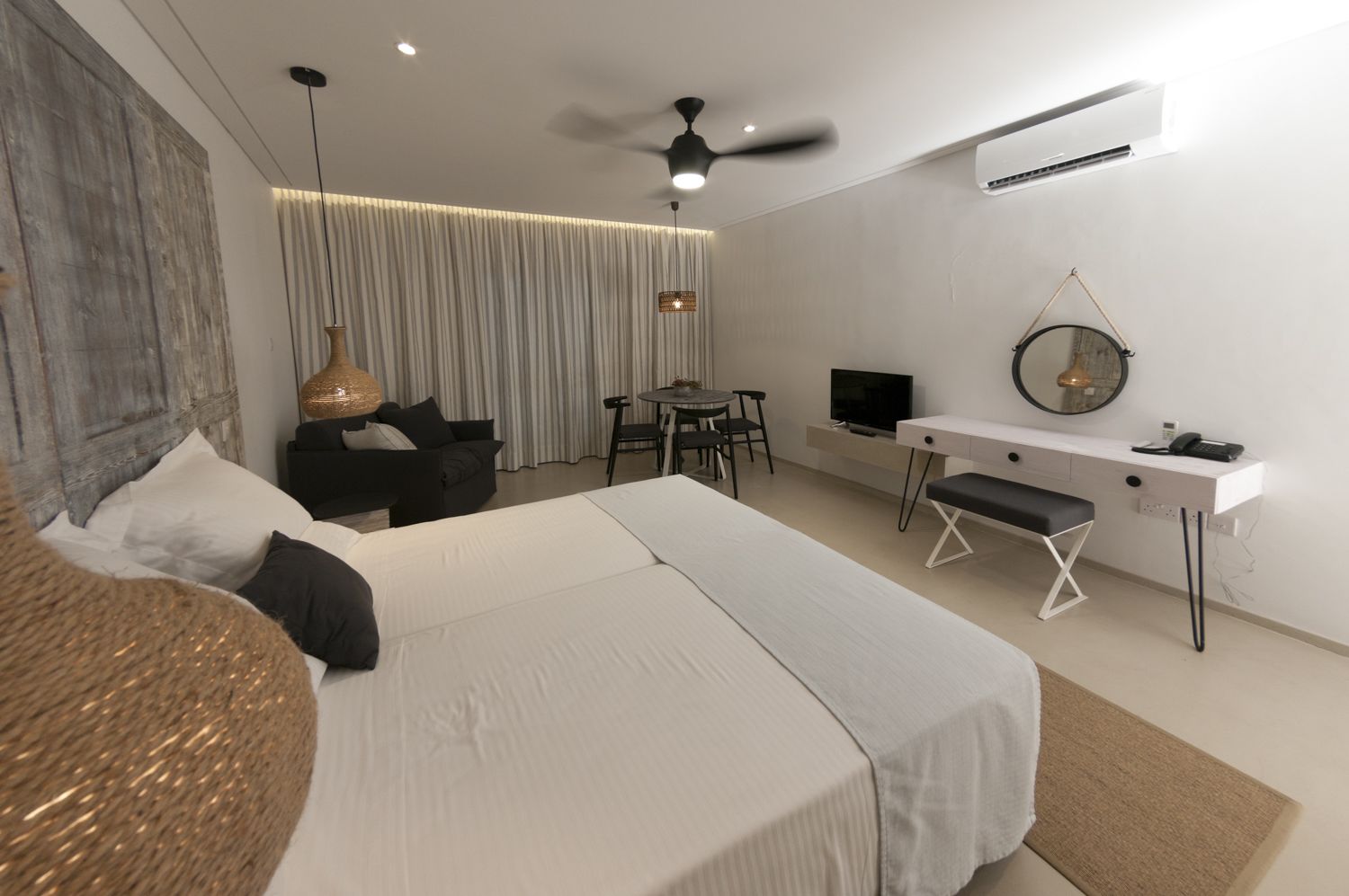 Et moderne hotelværelse med en stor seng, et skrivebord, en stol, et fjernsyn og en ventilator.
