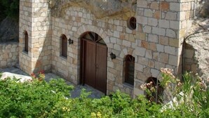 A stone chapel with a cross on top, set against a hillside with greenery. - Hylatio Tourist Village (Pissouri)