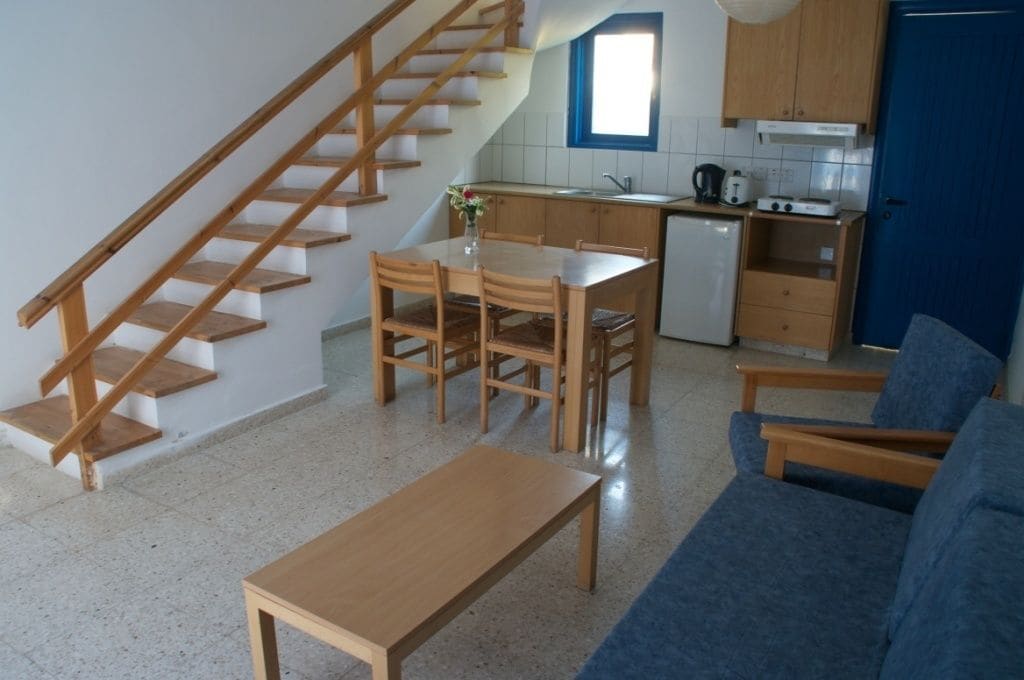 Ein kompakter Wohnraum mit einer Holztreppe, einem Essbereich inklusive Tisch und Stühlen, einer Küchenzeile und einem blauen Sofa.