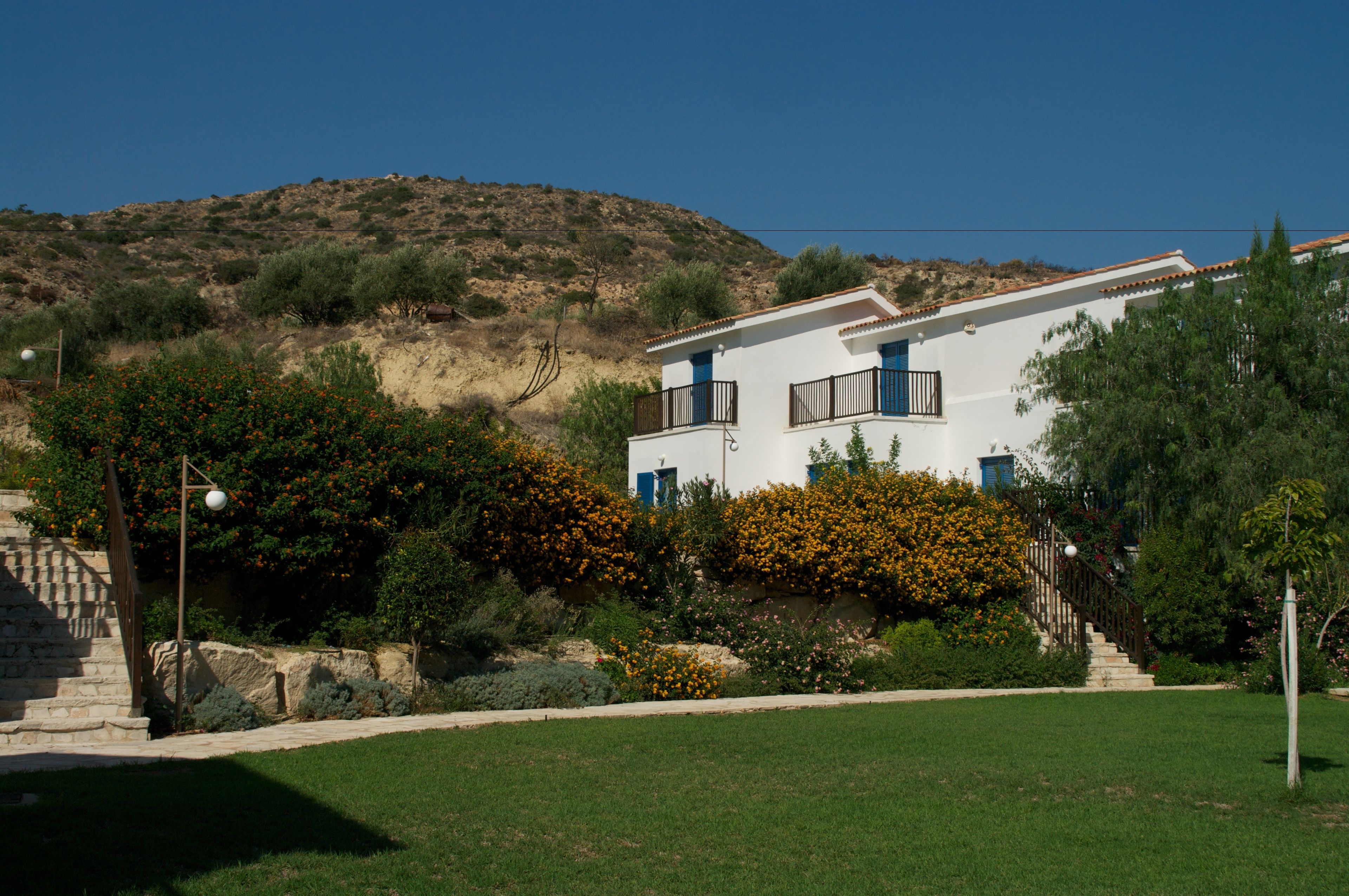 Una casa moderna de dos pisos con fachada blanca, contraventanas azules y una escalera de piedra que conduce a la entrada.