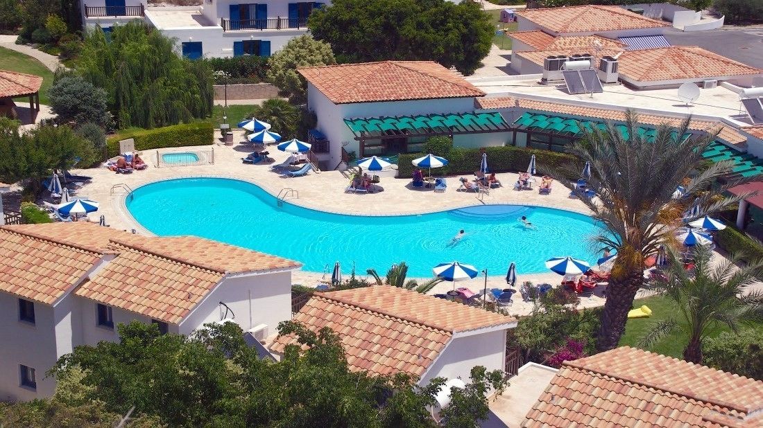 A pool area with multiple sunbathing spots and umbrellas, surrounded by buildings with tiled roofs.