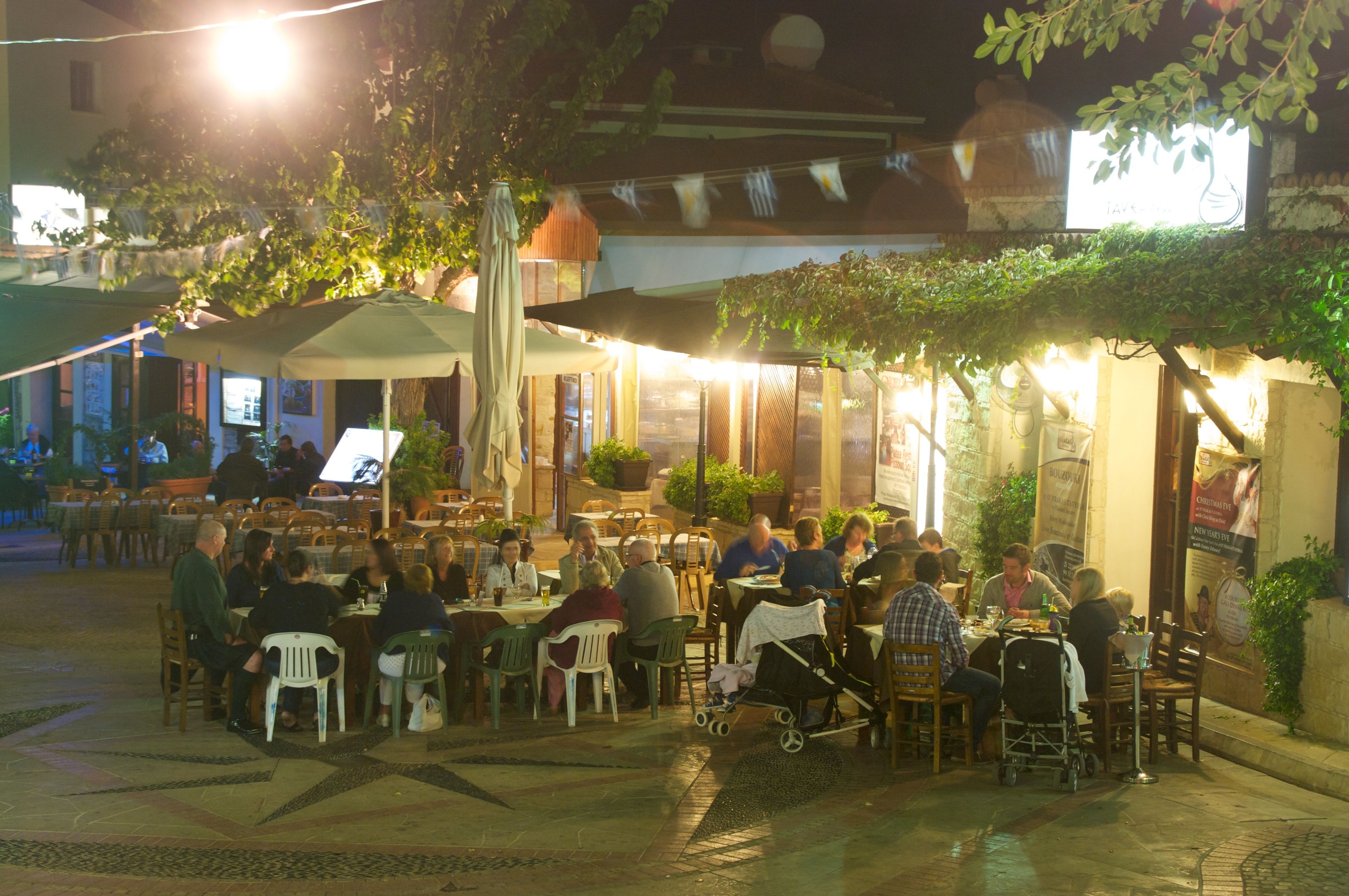 Un espacio de comedor al aire libre con mesas y sillas, rodeado de follaje y cubierto por una pérgola.