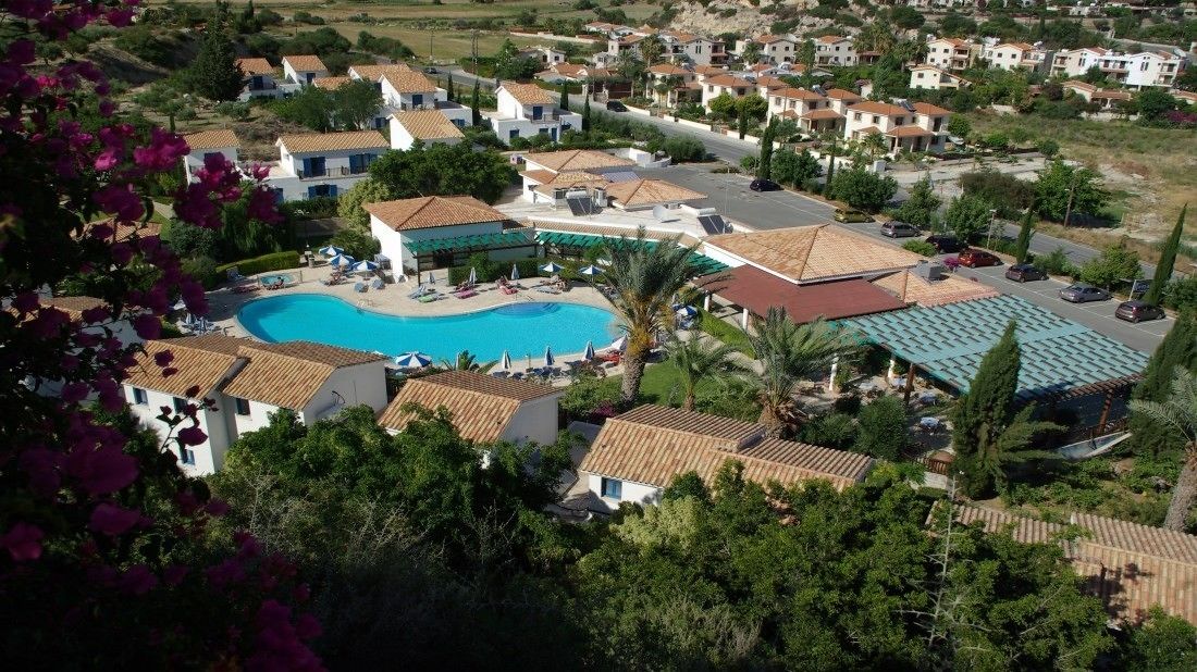 An aerial view of a resort with a swimming pool, villas, and a green landscape.