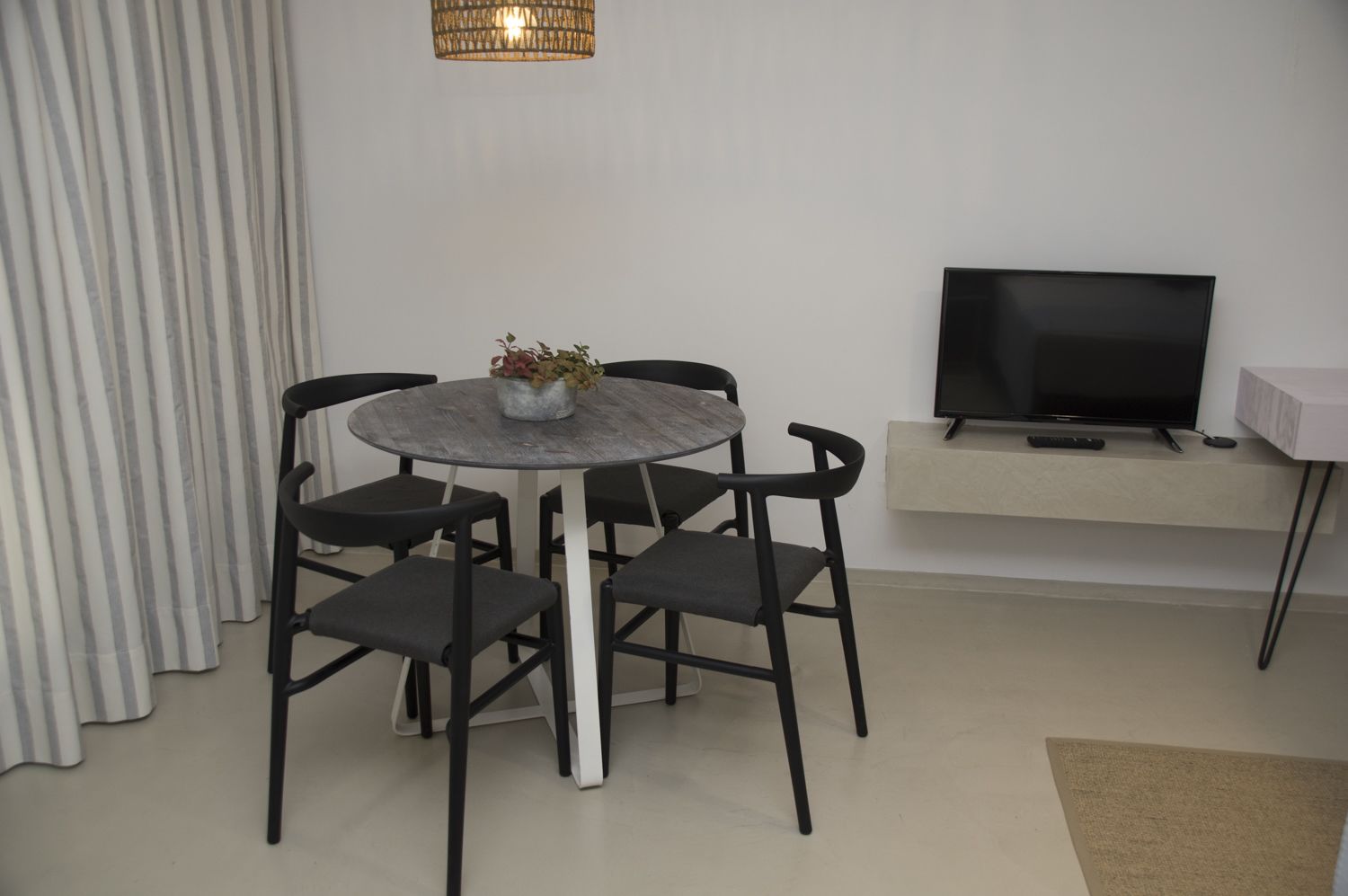 Un salon moderne avec une table ronde, quatre chaises, un téléviseur posé sur un meuble et une plante sur la table.