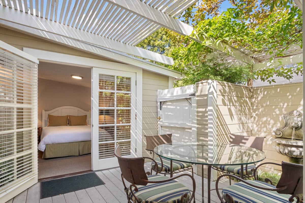 Une chambre à coucher avec un lit et une porte vitrée donnant sur une terrasse extérieure équipée d’une table et de chaises.