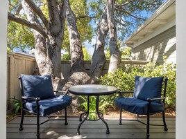 An outdoor patio with two blue chairs and a small round table.