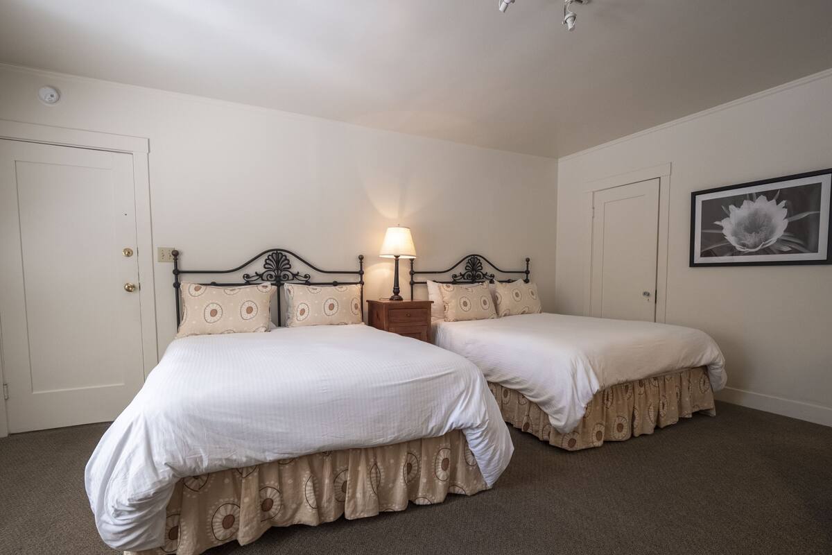 Une chambre avec deux lits, une table de chevet, une lampe et un tableau encadré au mur.