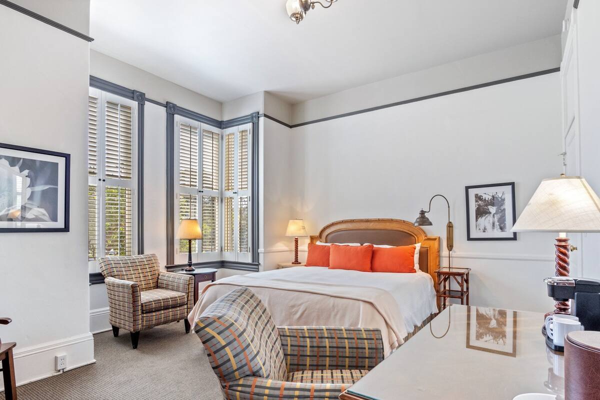 Une chambre d’hôtel avec un lit, deux chaises, un bureau et une lampe.
