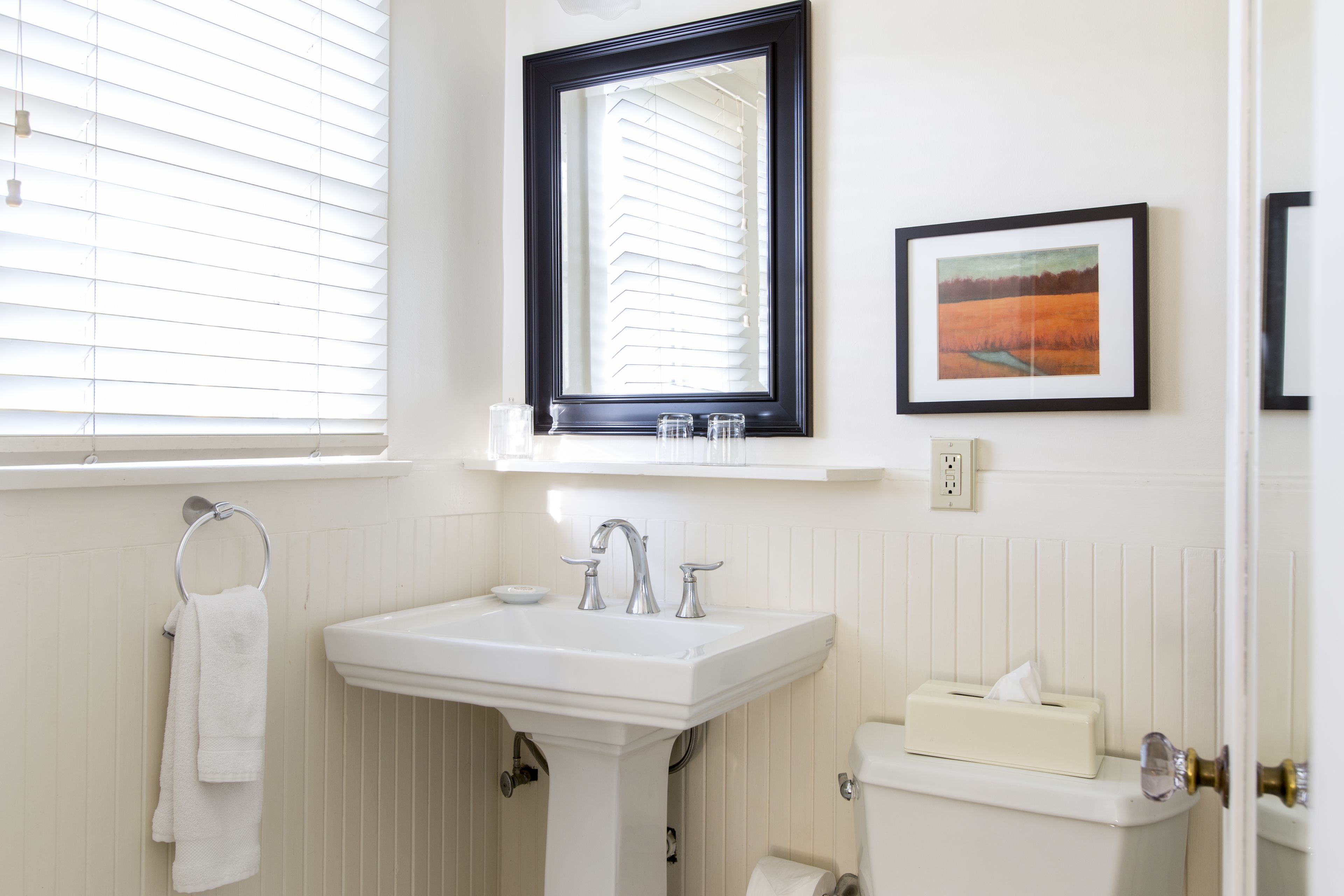 A bathroom with a white sink, a mirror, a toilet, and a window with blinds.