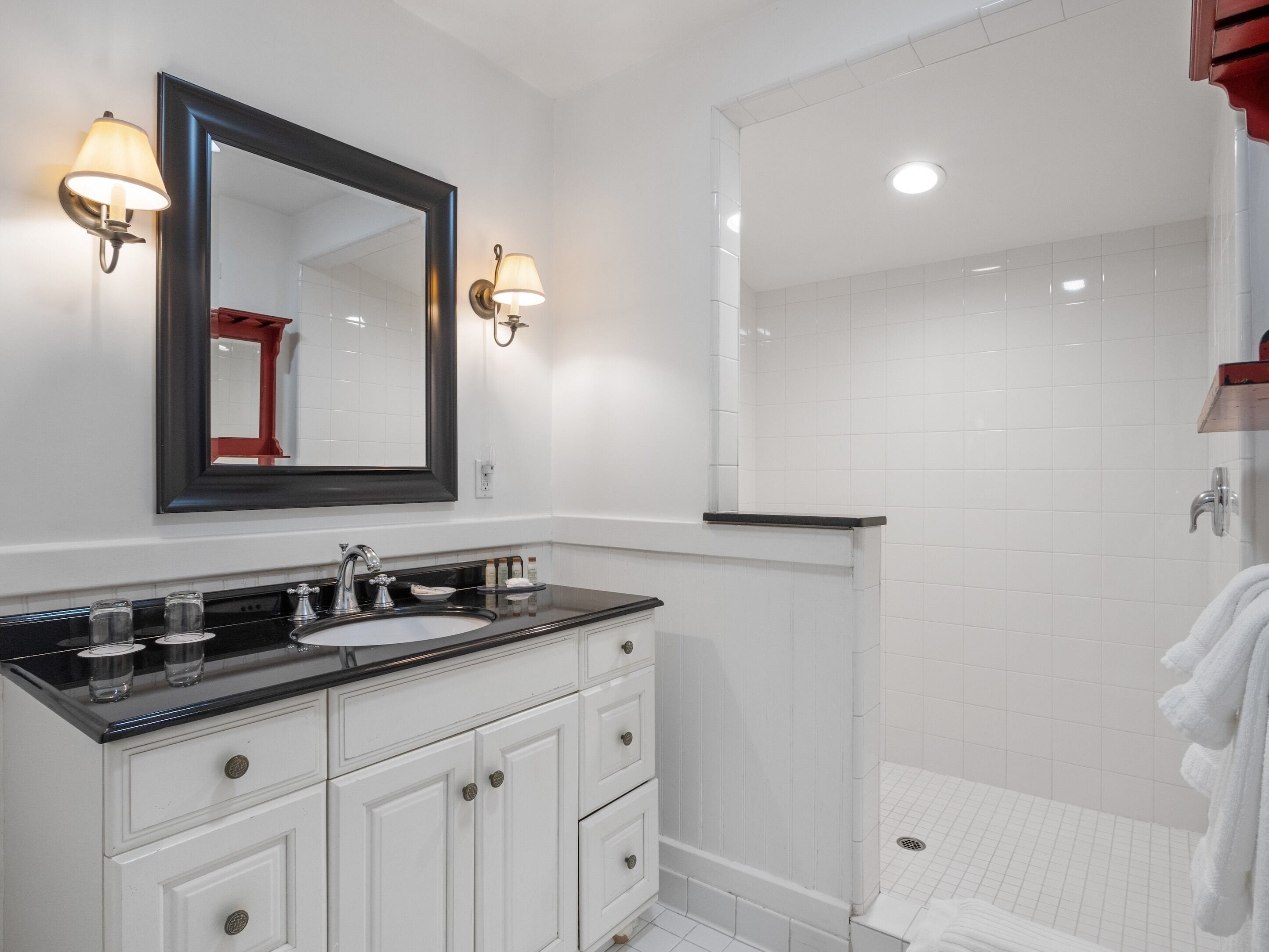 Une salle de bain moderne avec un lavabo sur un plan de toilette noir, des meubles blancs et un grand miroir.