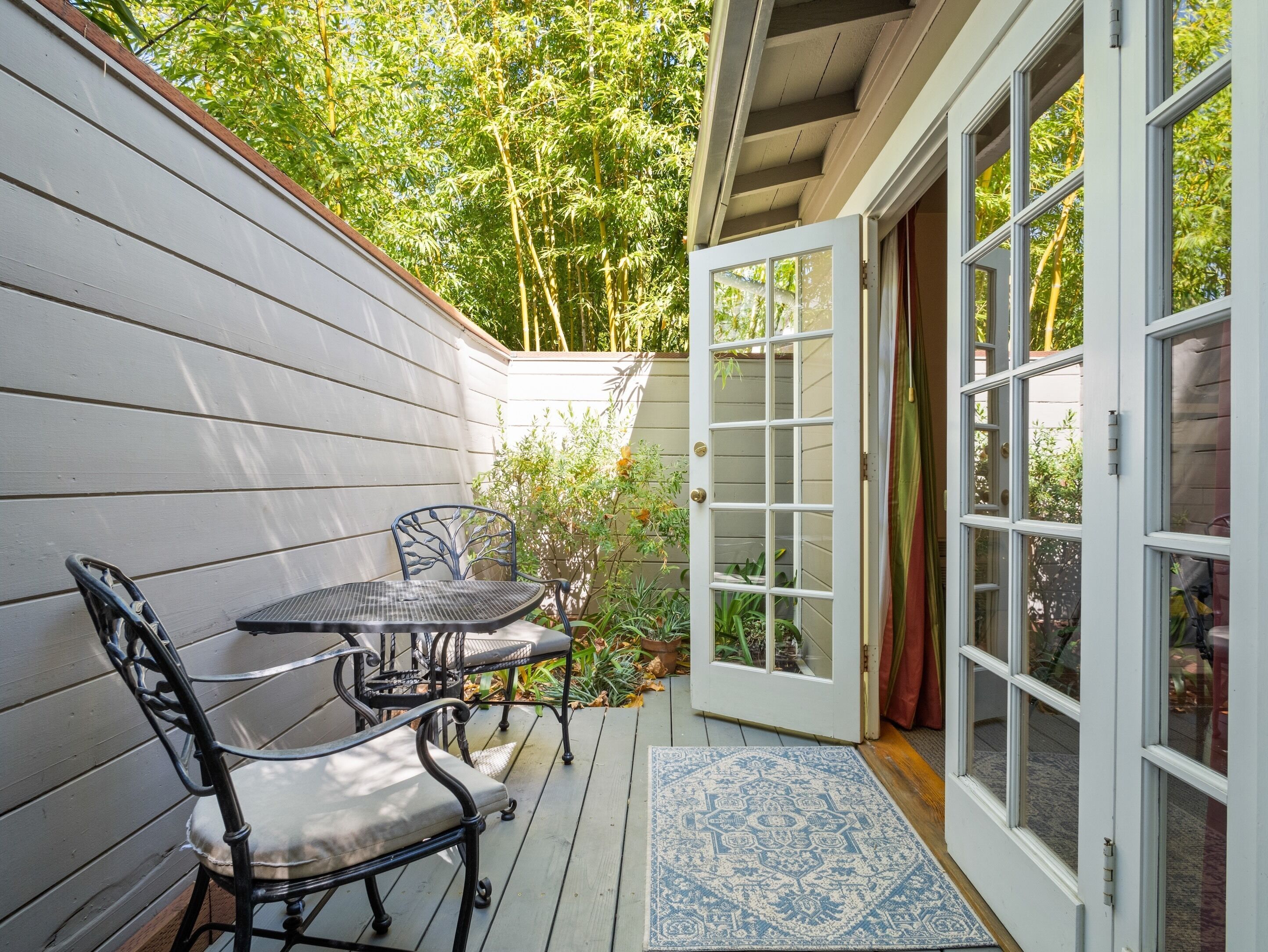 A patio with a table and chairs, a door leading to a garden, and a blue patterned rug.