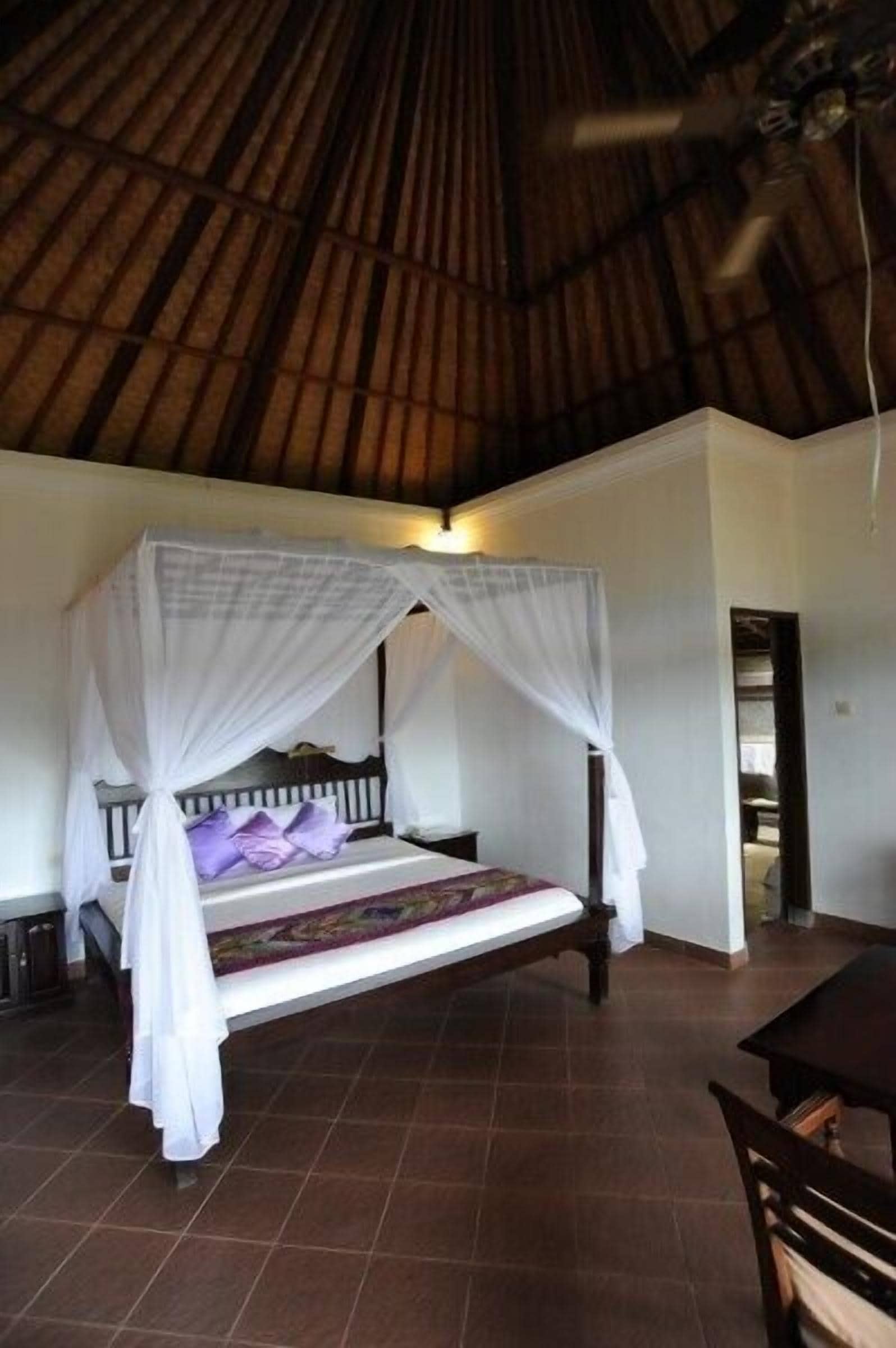 A room with a bed under a thatched roof, a wooden bench, and a table.