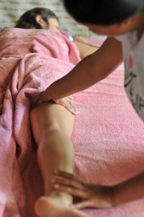 Una persona recostada en una cama con una manta rosa, recibiendo un masaje.