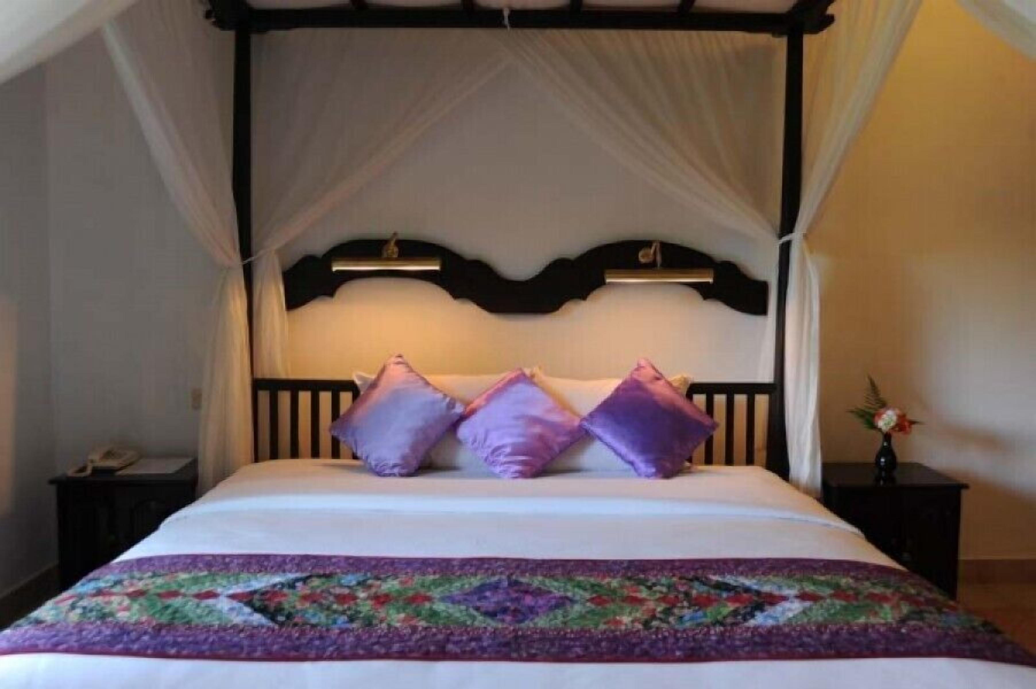 A four-poster canopy bed with a floral bedspread and three pillows.