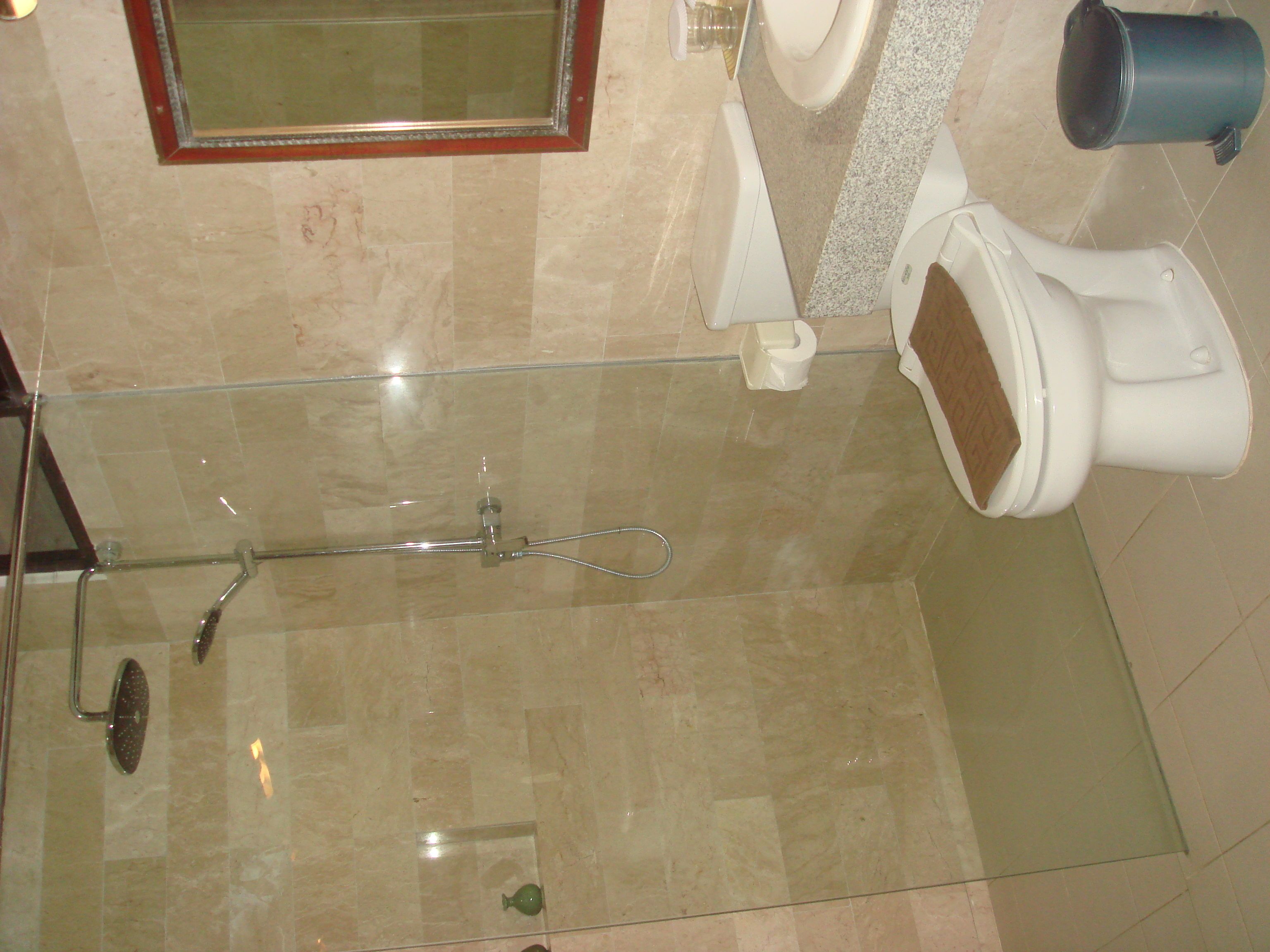 A bathroom with a glass shower enclosure, a toilet, and a trash can.