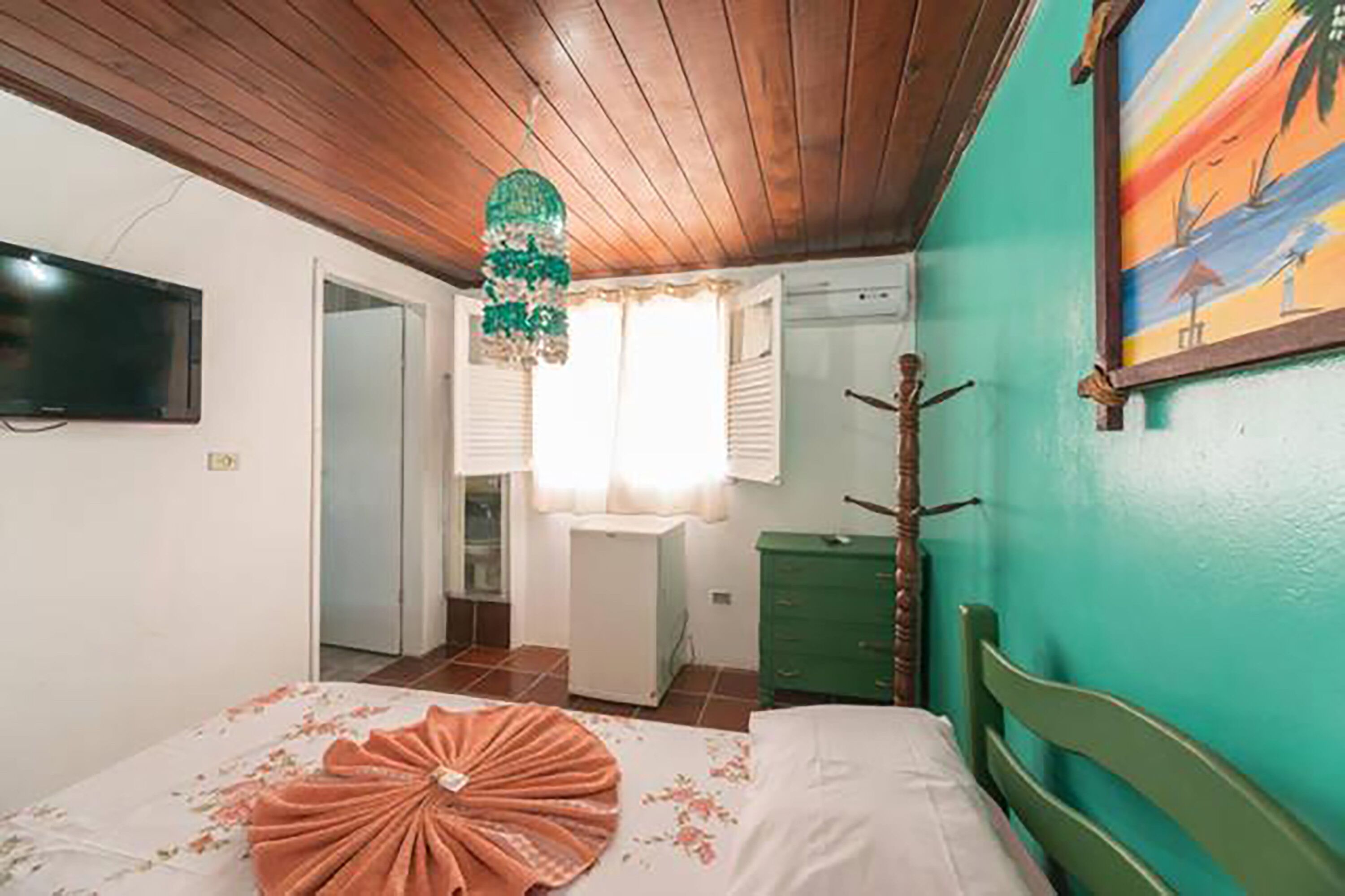 A bedroom with a bed, a television, a green dresser, and a painting on the wall.
