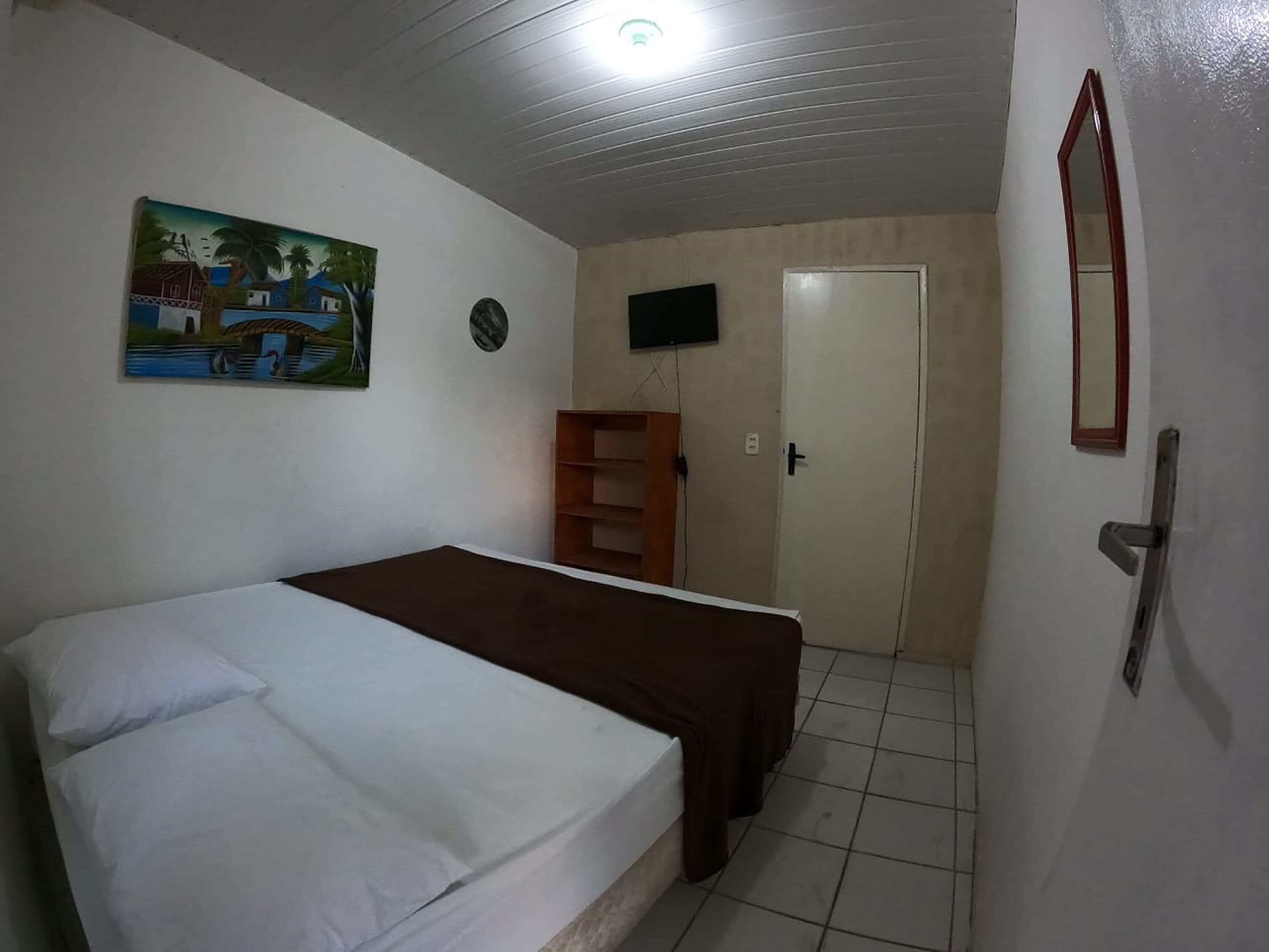 A bedroom with a bed, a TV mounted on the wall, a door, and a painting.