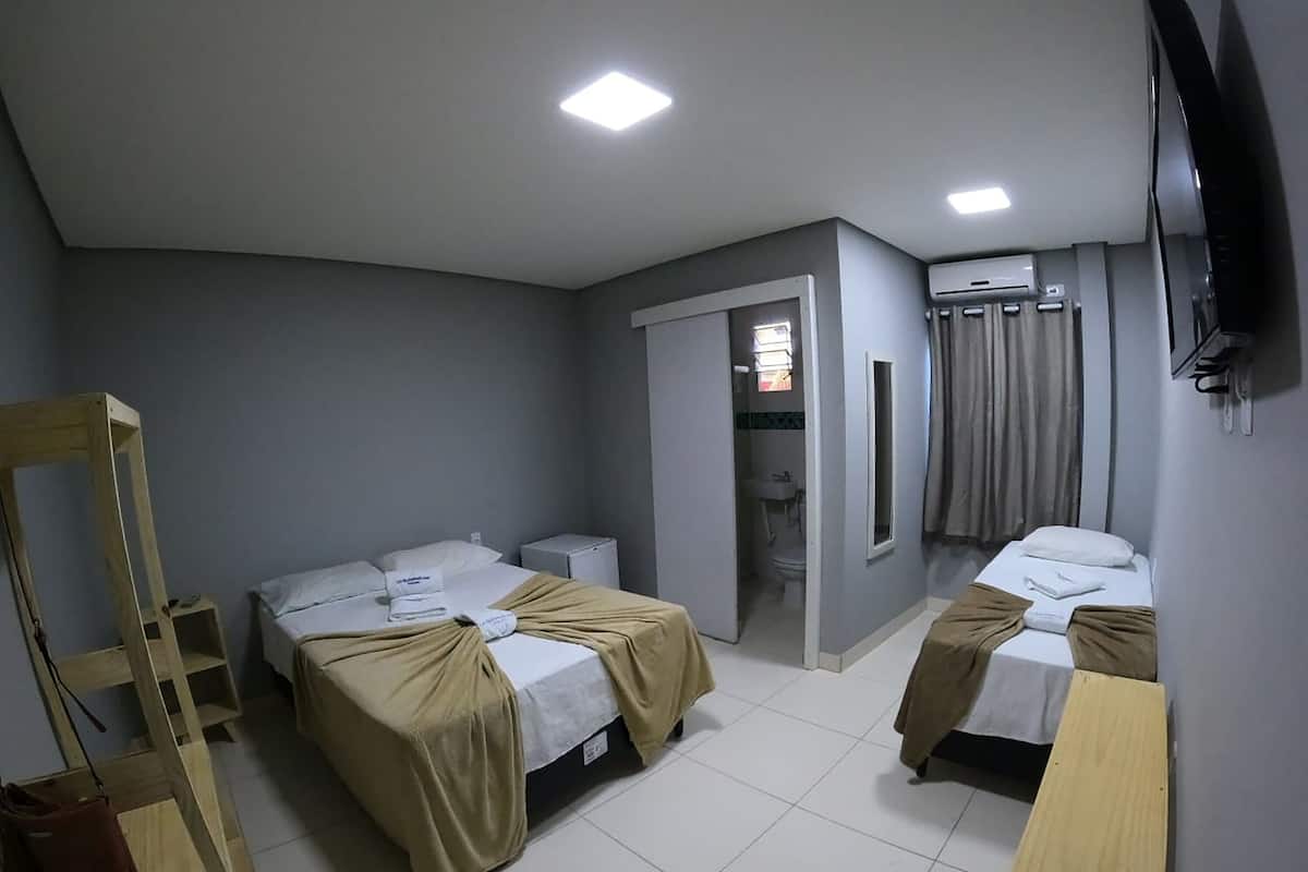 A hotel room with two beds, a wooden chair, a small table, a TV, and an air conditioning unit.