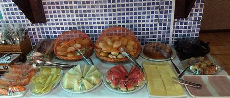 Un buffet proposant une variété d’aliments, notamment des fruits, du pain et des pâtisseries.
