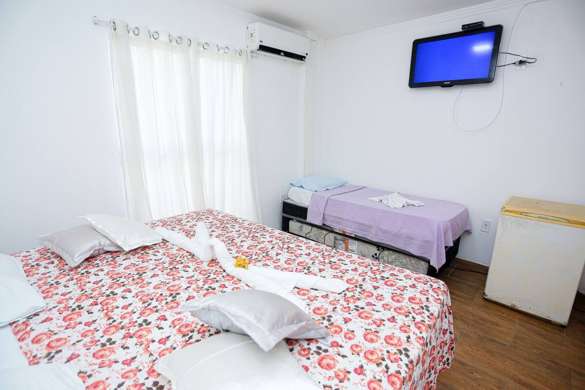 A bedroom with a bed, a TV, a small table, and a refrigerator.