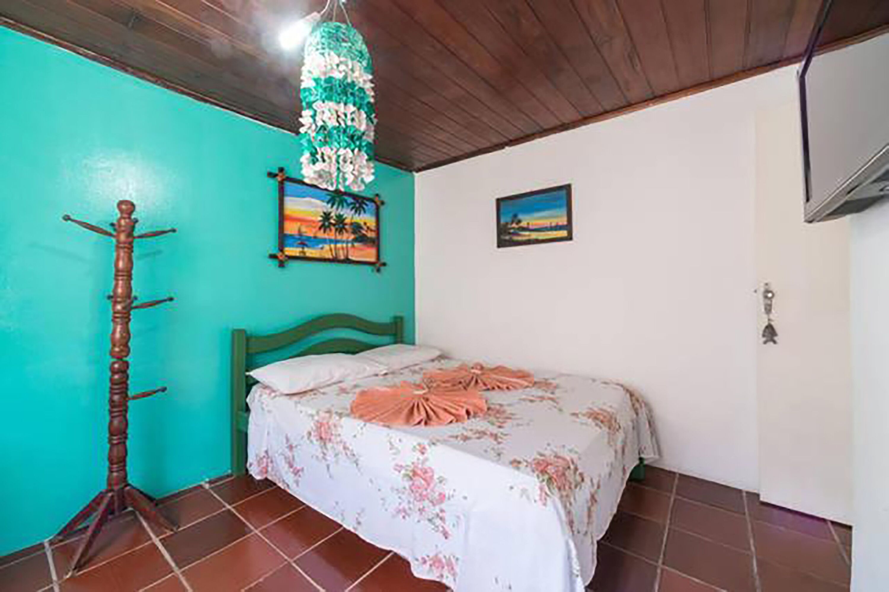 A bedroom with a bed, a wooden coat rack, a teal wall, and a painting.