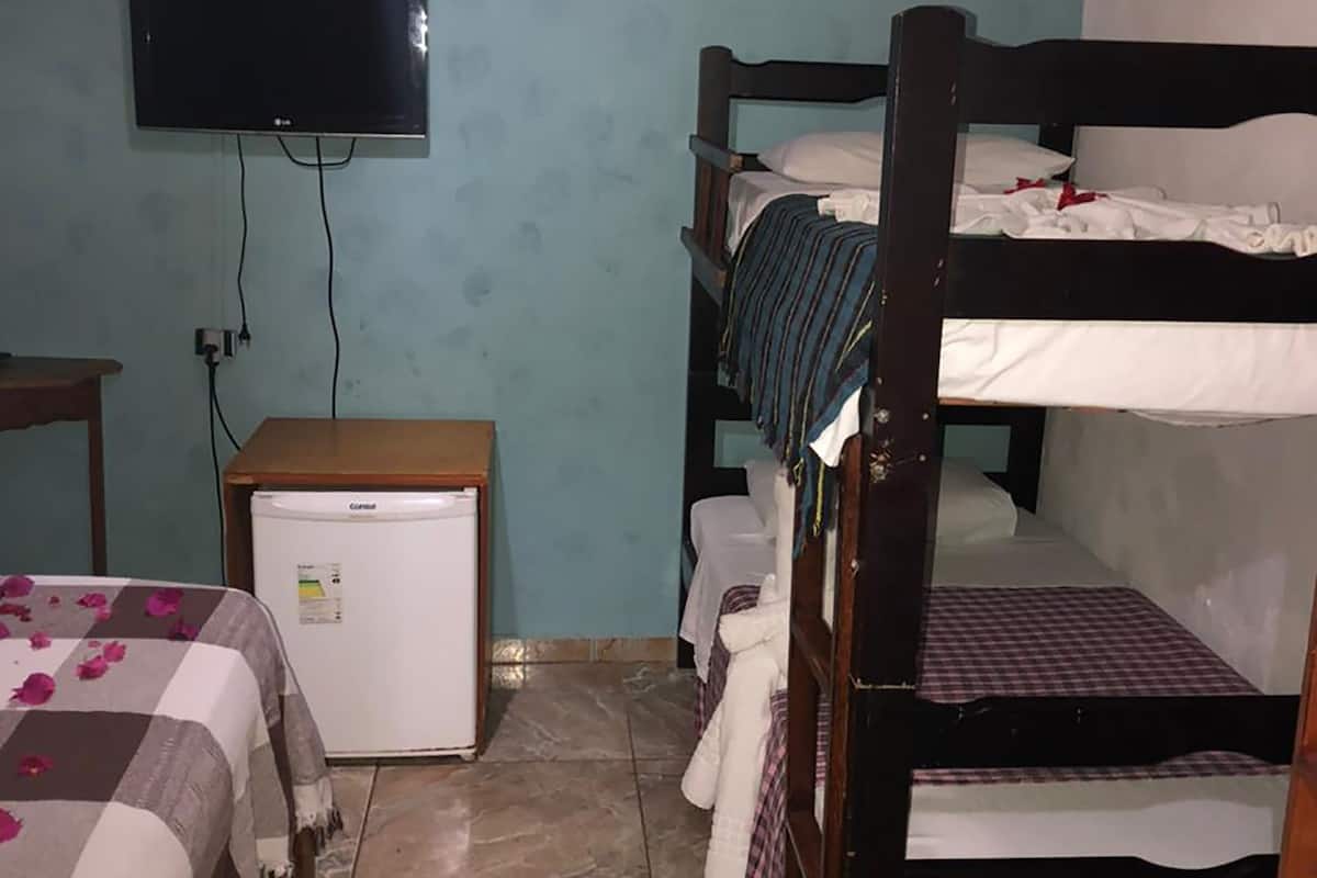 A small, compact room with a bunk bed, a television mounted on the wall, a small refrigerator, and a tiled floor.