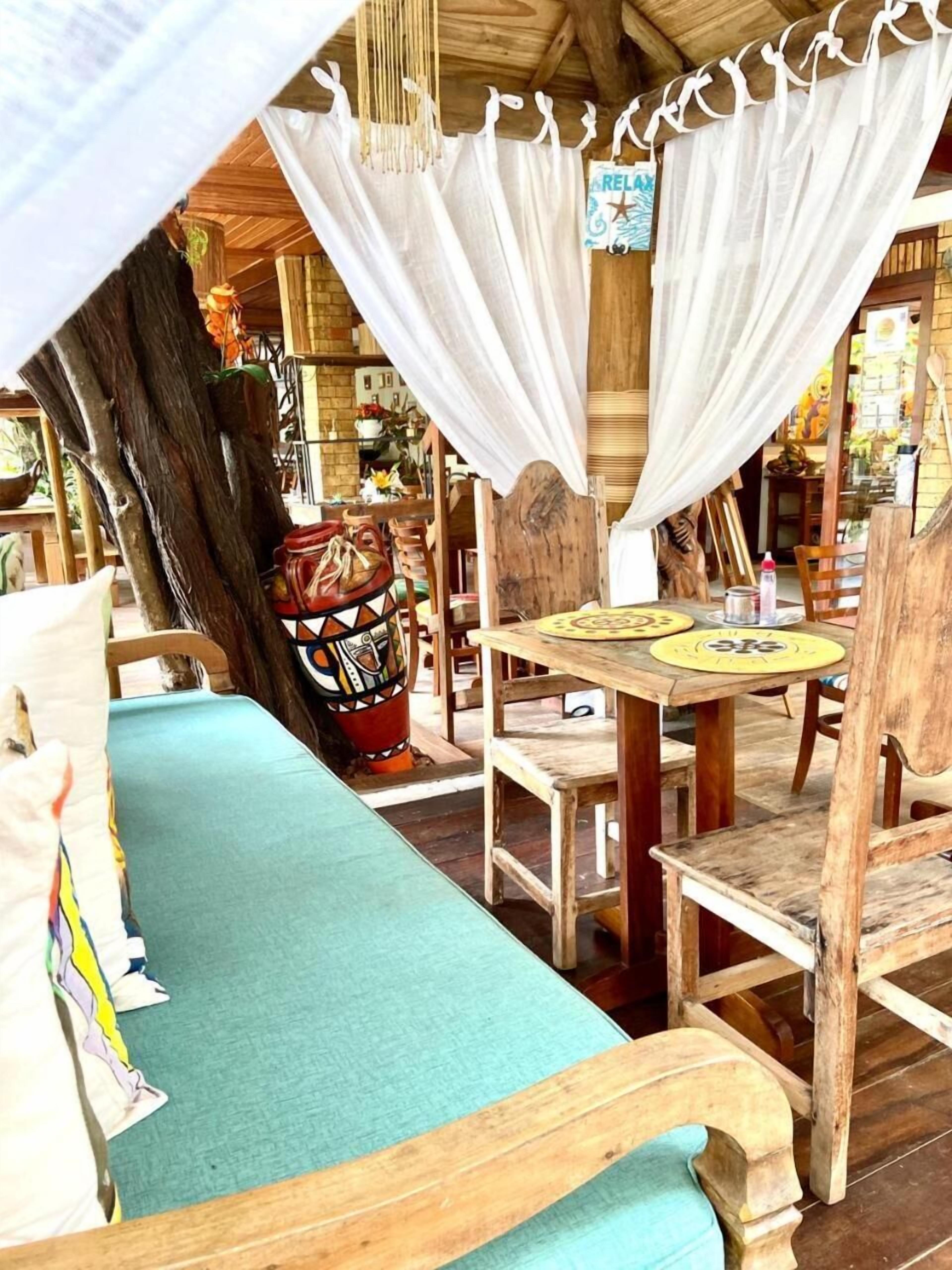 A rustic wooden room with a bed, a table, and chairs. There is a sign with the word "RELAX" on the wall.