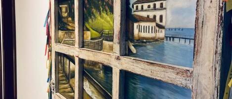 A wall with a rustic wooden frame containing multiple paintings depicting a coastal scene with a building and pier.
