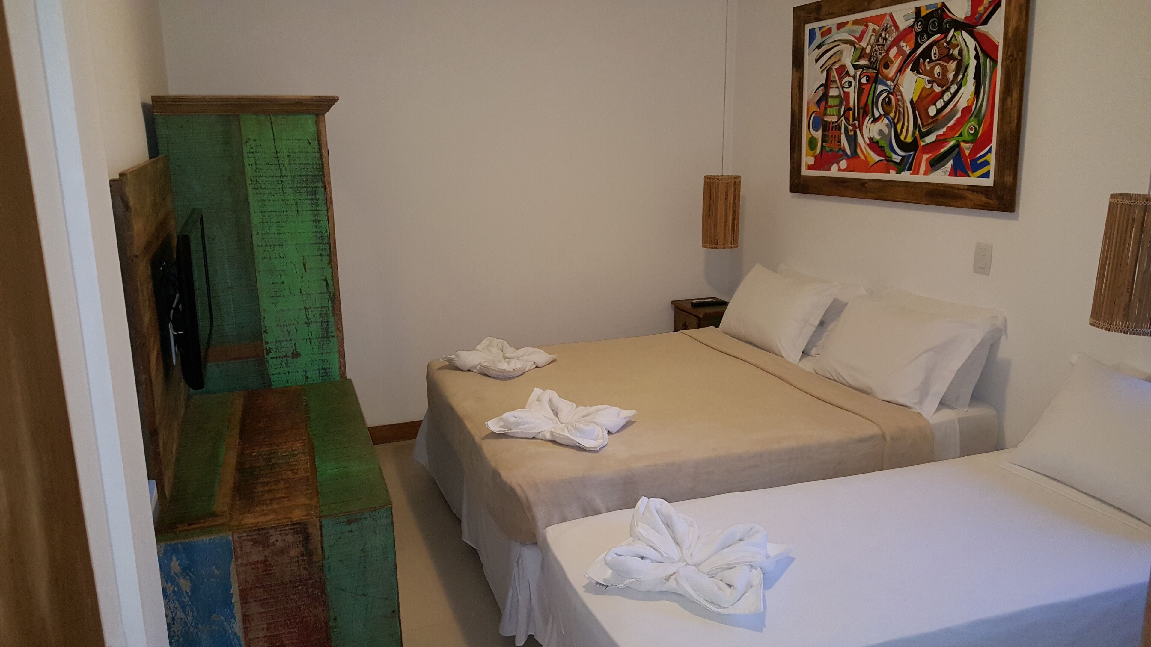 A hotel room with two beds, a green cabinet, a painting on the wall, and a wooden bench.
