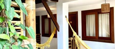 Un balcón de madera con una hamaca, una escalera y vistas del entorno.