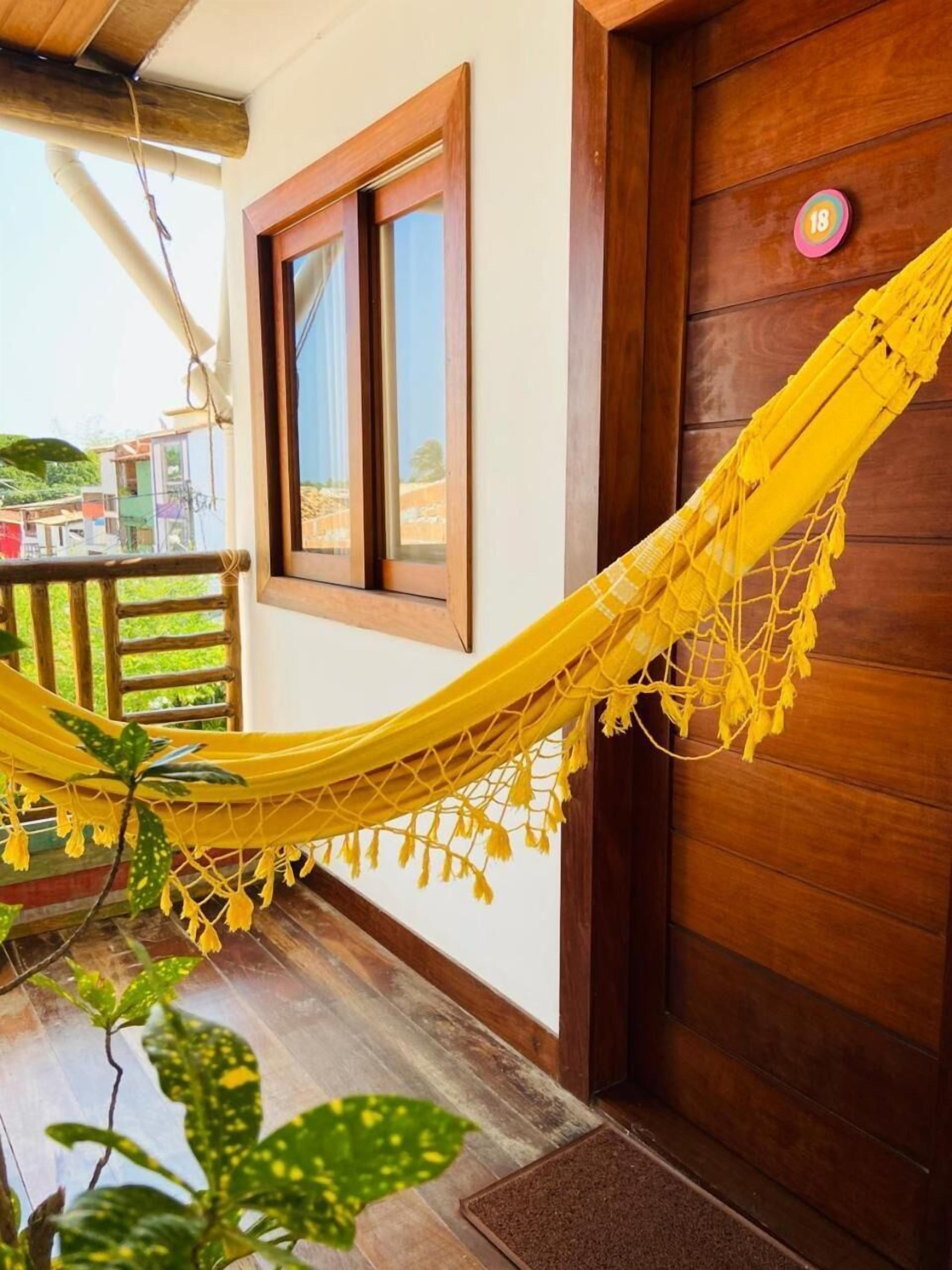 A yellow hammock on a wooden porch with a wooden door and a window.