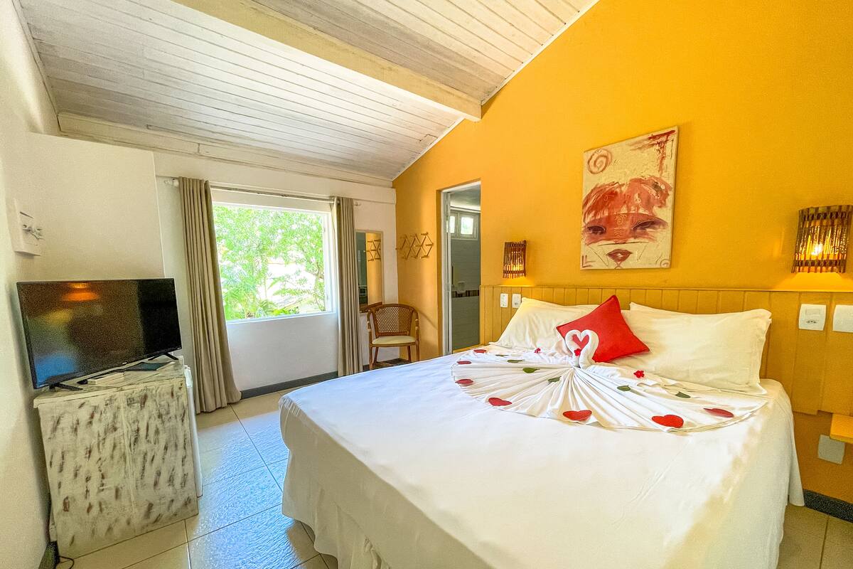 Een hotelkamer met een bed, een televisie op een bijzettafeltje, een raam met gordijnen en een schilderij aan de muur.