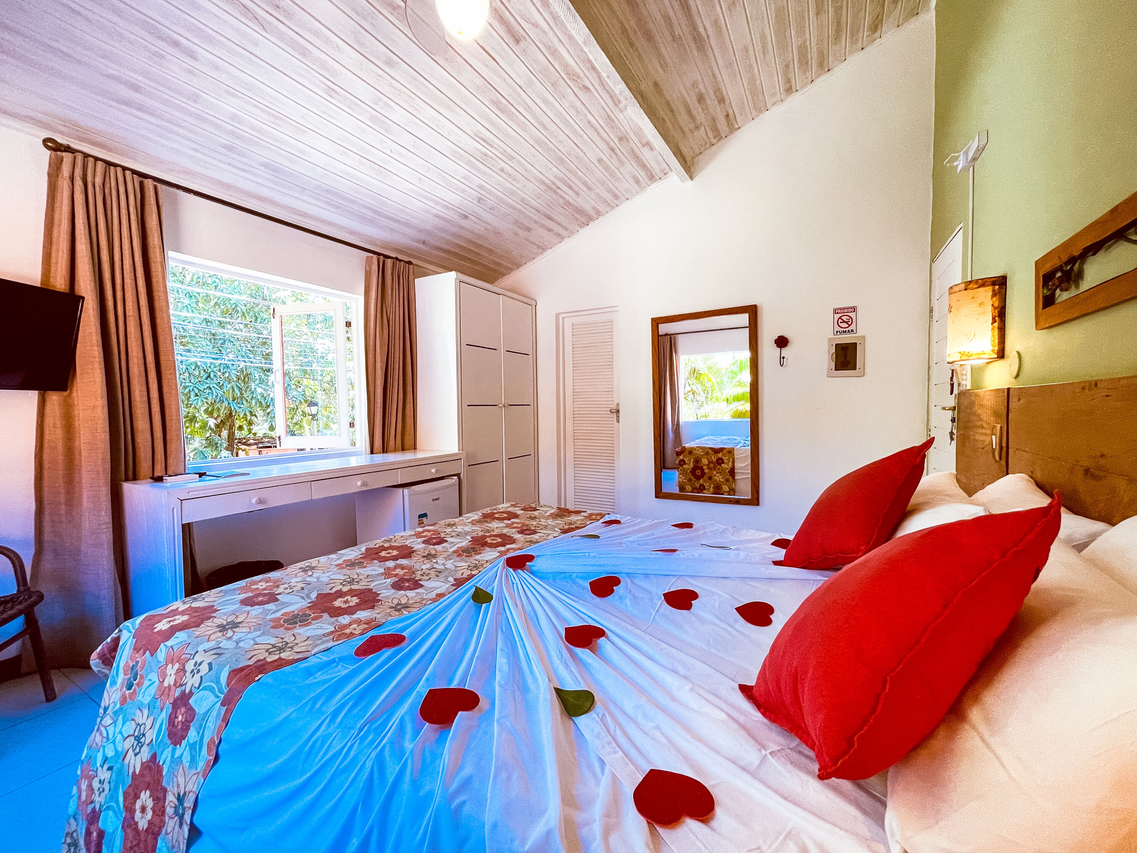 A bedroom with a bed, a desk, a mirror, and a window.