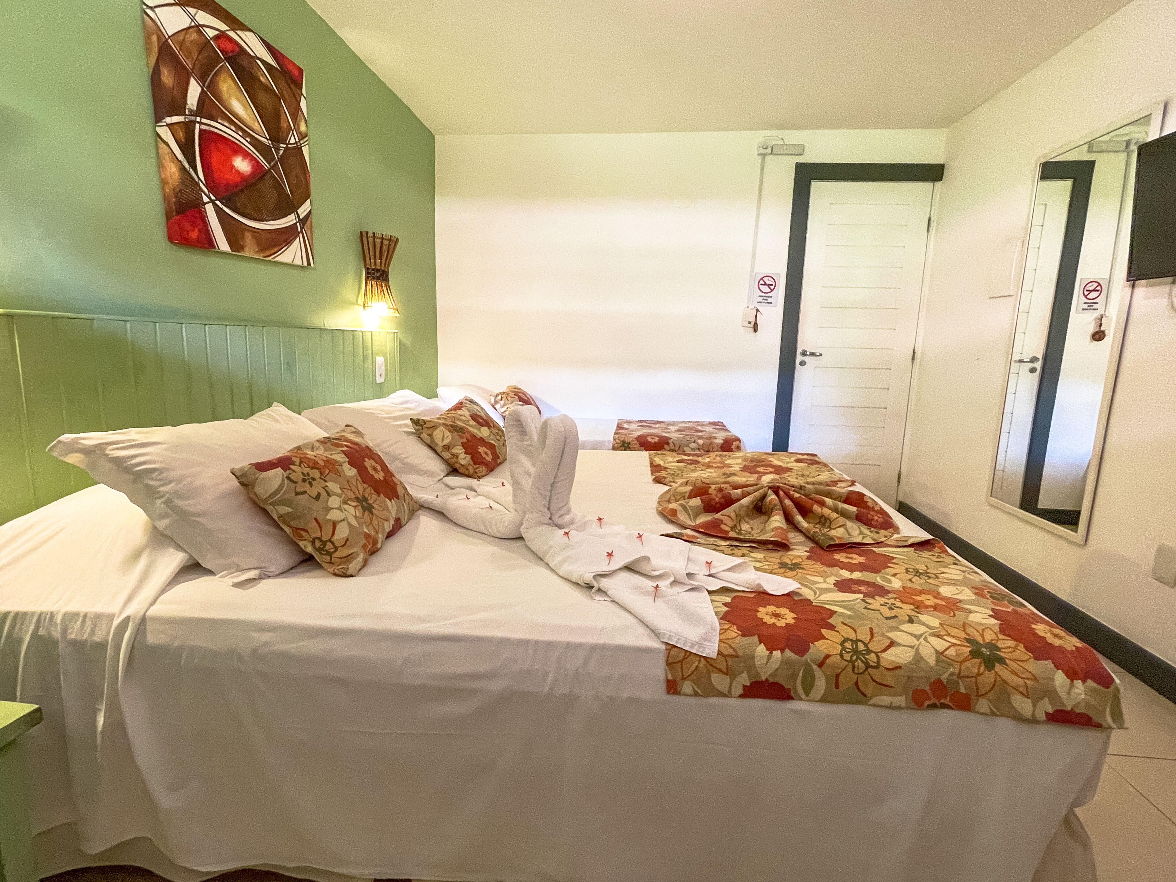 Ett hotellrum med en säng, ett blommigt sängöverkast och ett konstverk som hänger på väggen.