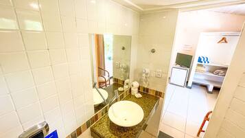 A bathroom with white tiles, a sink, a mirror, a hairdryer, and a shelf with towels.