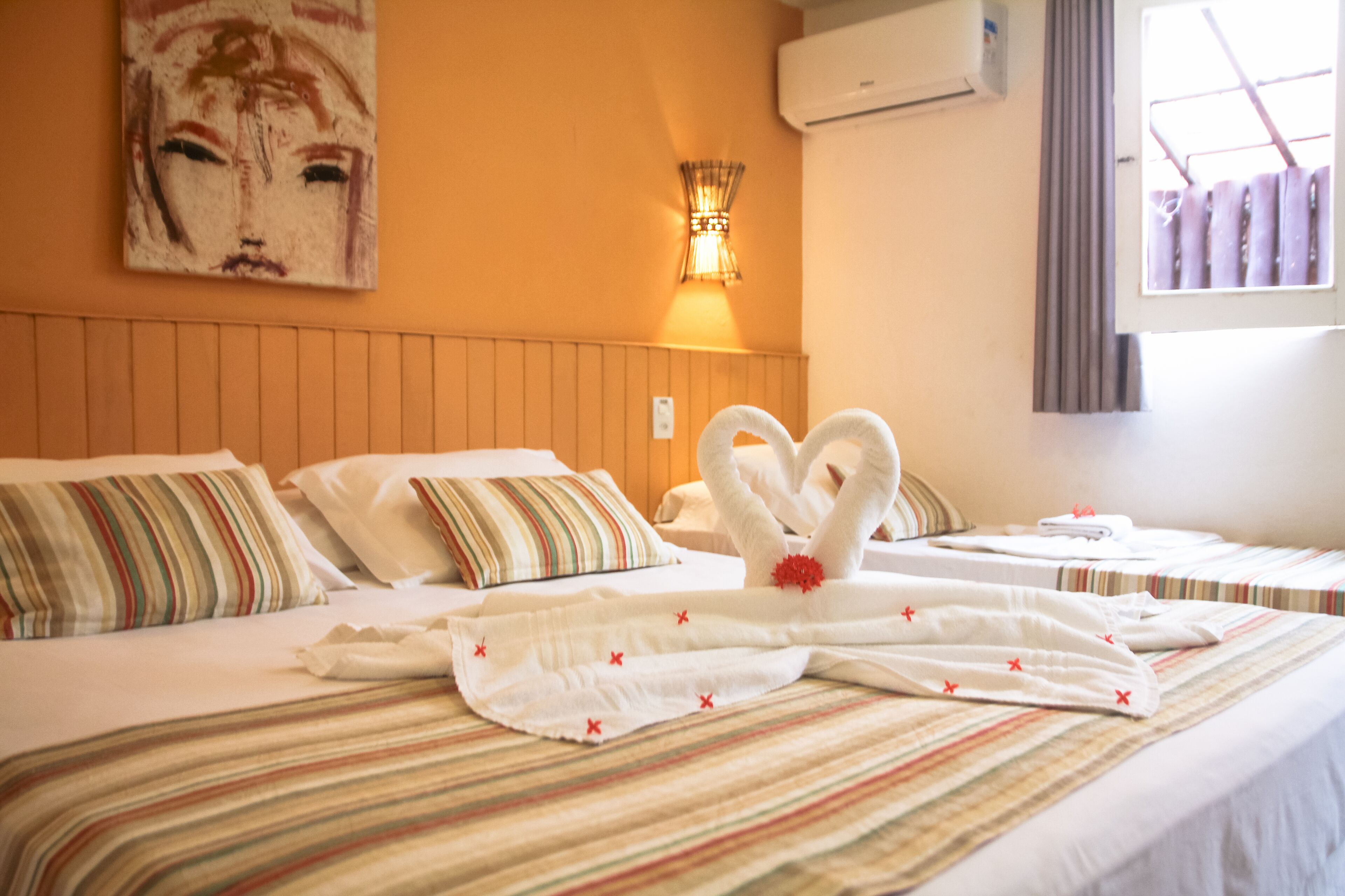 A hotel room with a bed featuring striped bedding, a wall-mounted air conditioner, and a painting above the bed.