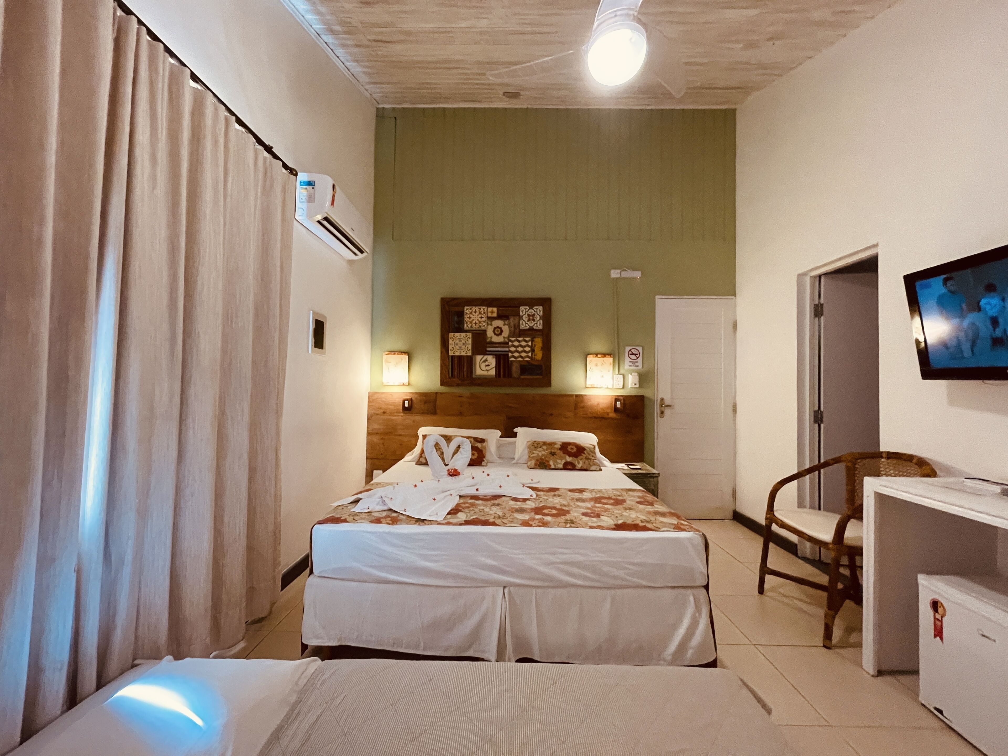 A hotel room with a bed, a desk, a chair, a television, and a wall-mounted air conditioner.