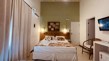 A hotel room with a bed, a desk, a chair, a television, and a wall-mounted air conditioner.