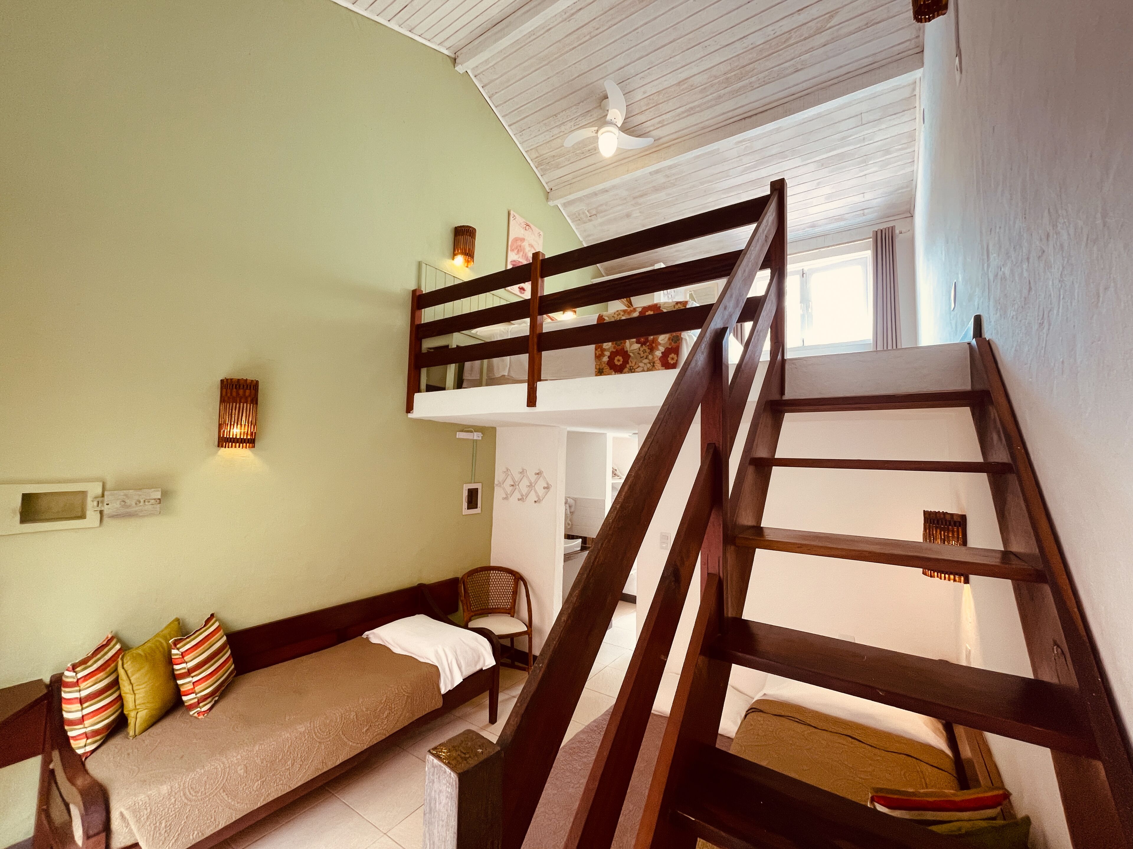 Una habitación con una cama litera, un sofá con cojines a rayas, una escalera de madera y un ventilador de techo.