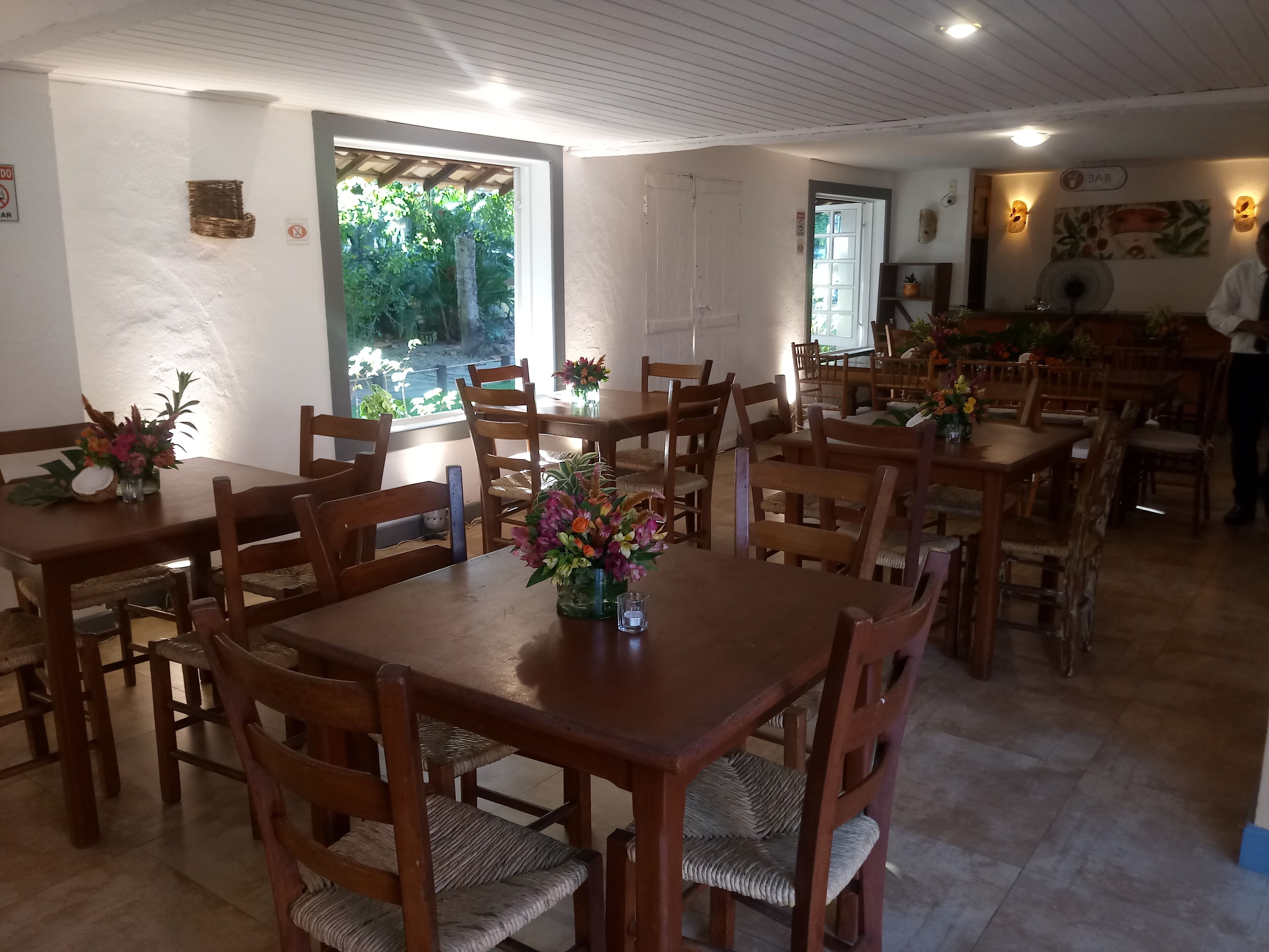 A dining area with wooden tables and chairs, some with floral centerpieces.