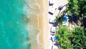 Een strand met witte parasols en ligstoelen, palmbomen en helder turquoise water.
