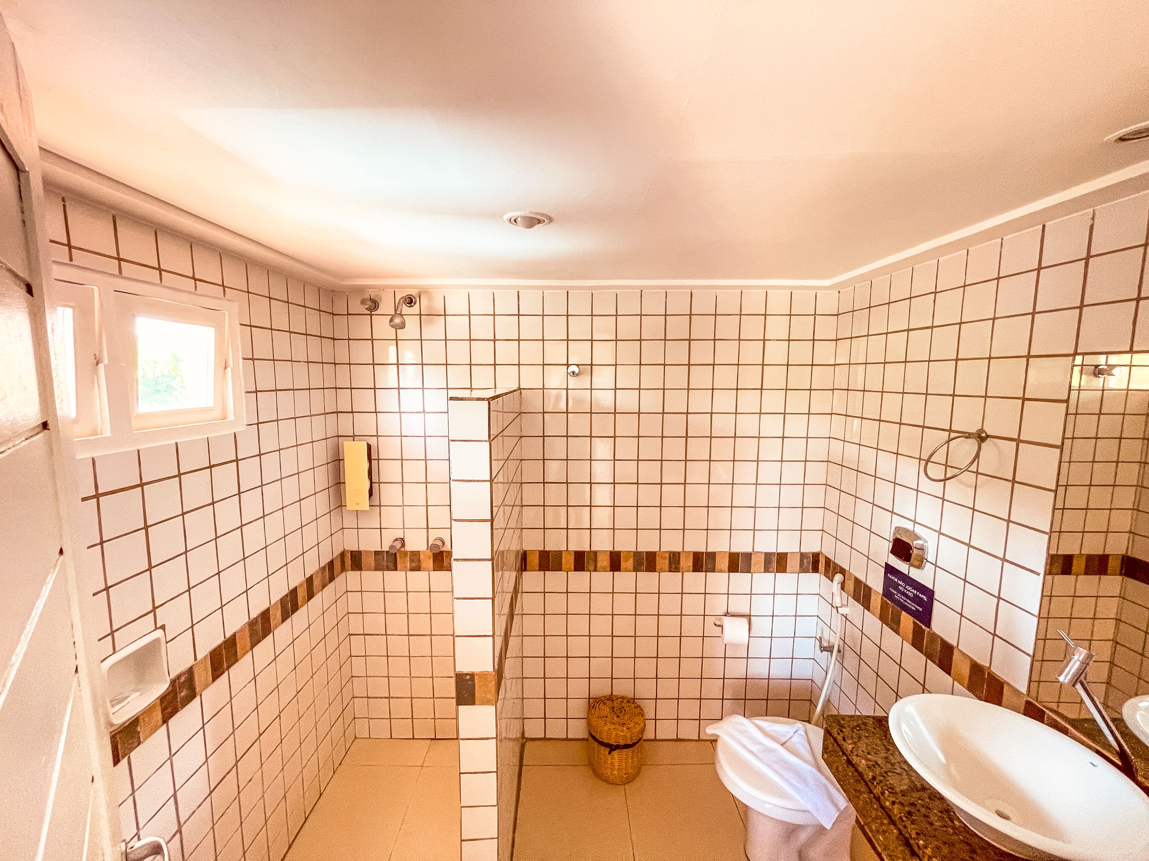 Un baño con paredes de azulejos blancos, ducha, inodoro y lavabo.