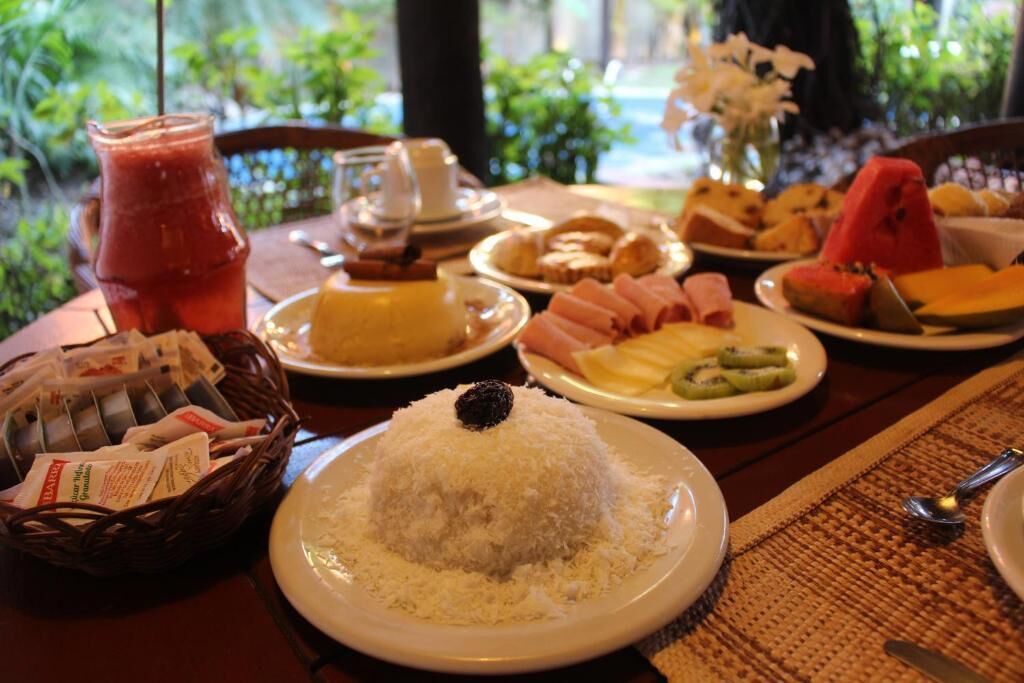 Une table dressée avec divers plats, notamment du riz, des fruits et des pâtisseries, ce qui laisse supposer qu’il s’agit d’un petit-déjeuner.