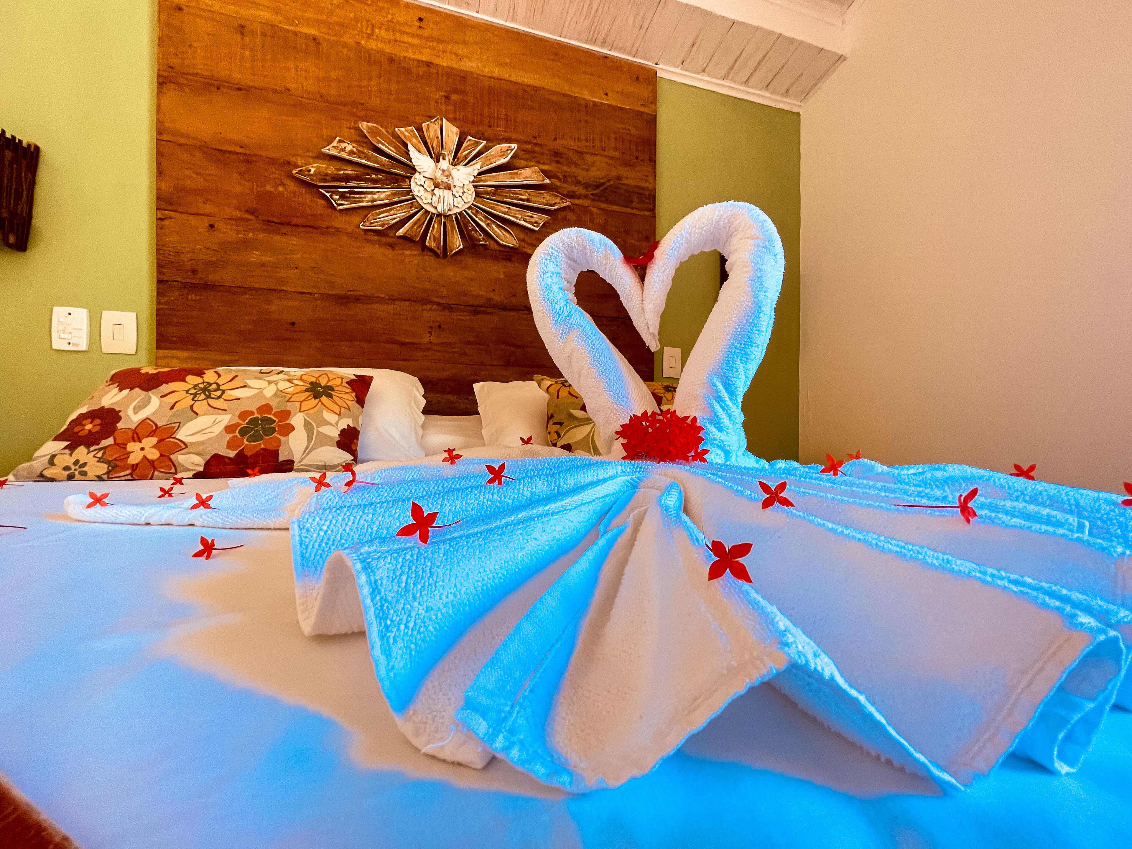 Een hotelkamer met een bed, een handdoekenfiguur in de vorm van een konijn, een houten hoofdbord en een decoratieve zonneslinger spiegel.