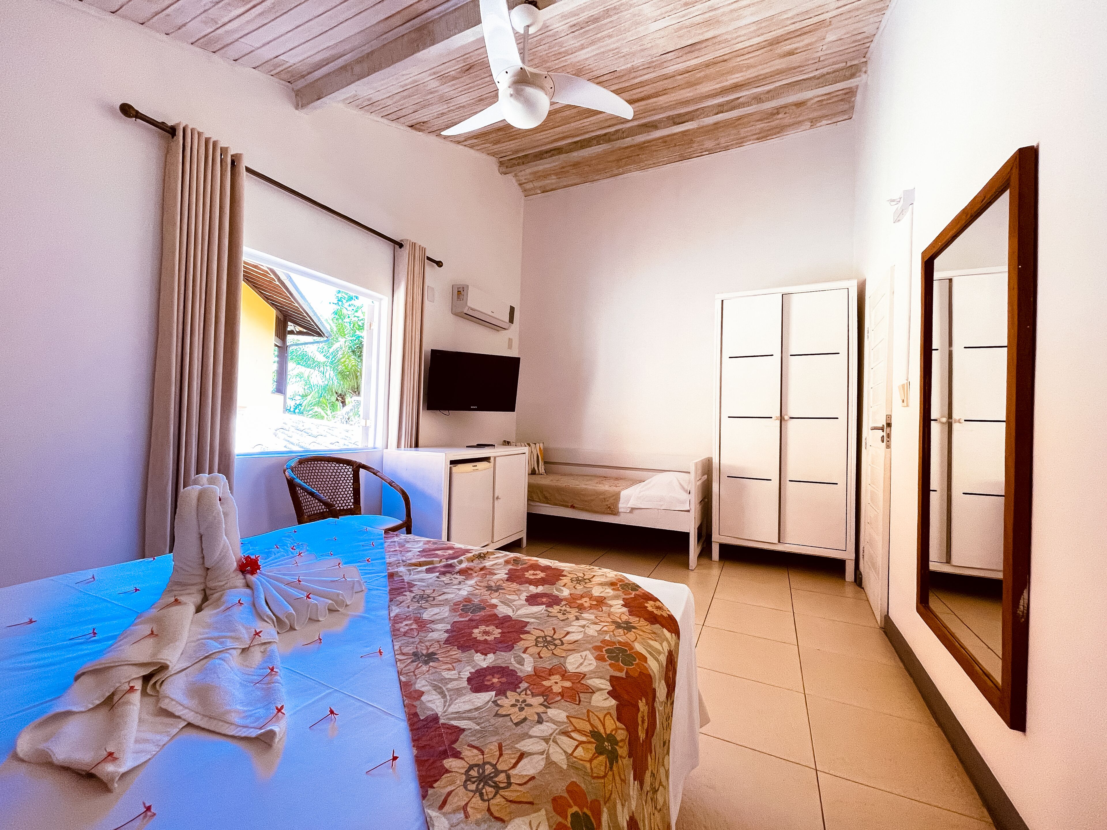 Ein Schlafzimmer mit Bett, Schreibtisch, Stuhl, Kleiderschrank, Fernseher und einem Fenster mit Vorhängen.
